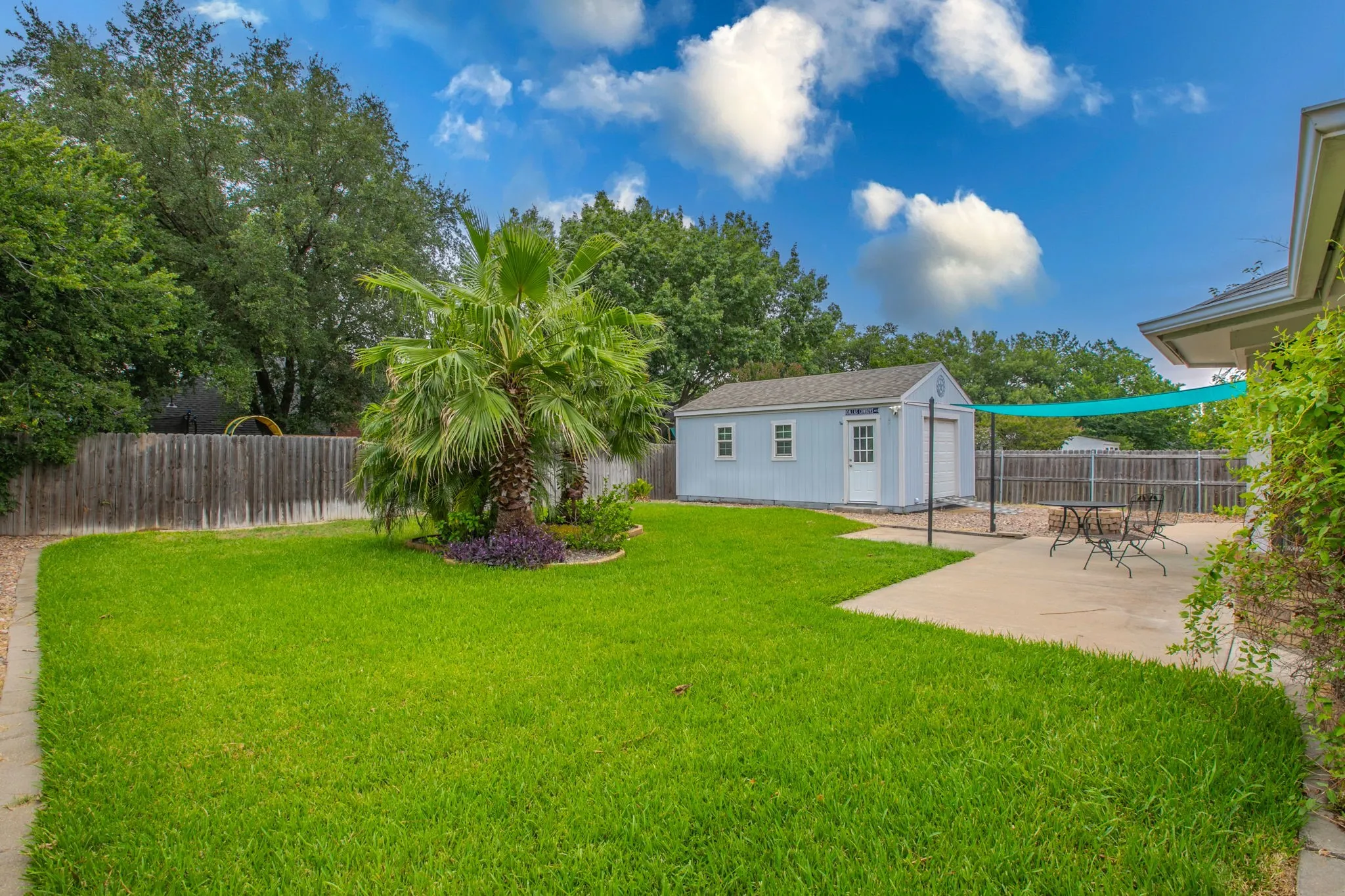 Spacious backyard featuring a manicured lawn, a detached storage shed with a roll-up door, mature trees, a privacy fence, and a concrete patio
