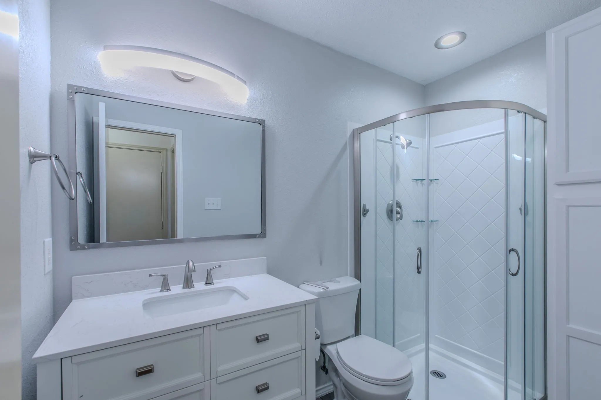 Updated bathroom featuring a corner shower with glass enclosure, white vanity with stone countertop, rectangular undermount sink, contemporary faucet, and recessed lighting