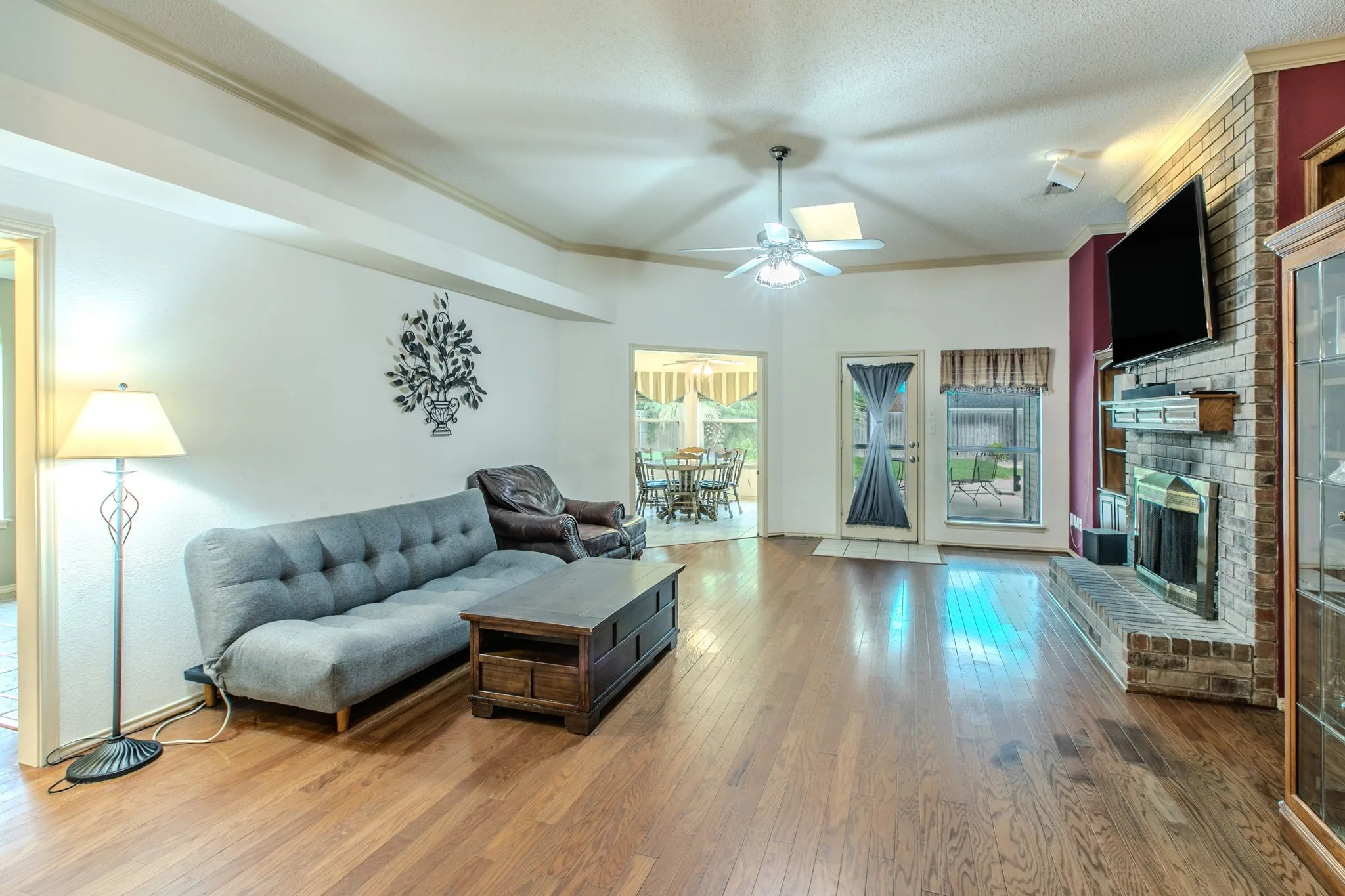 Spacious living area featuring wood-finish flooring, a brick fireplace with a mantle, and a ceiling fan