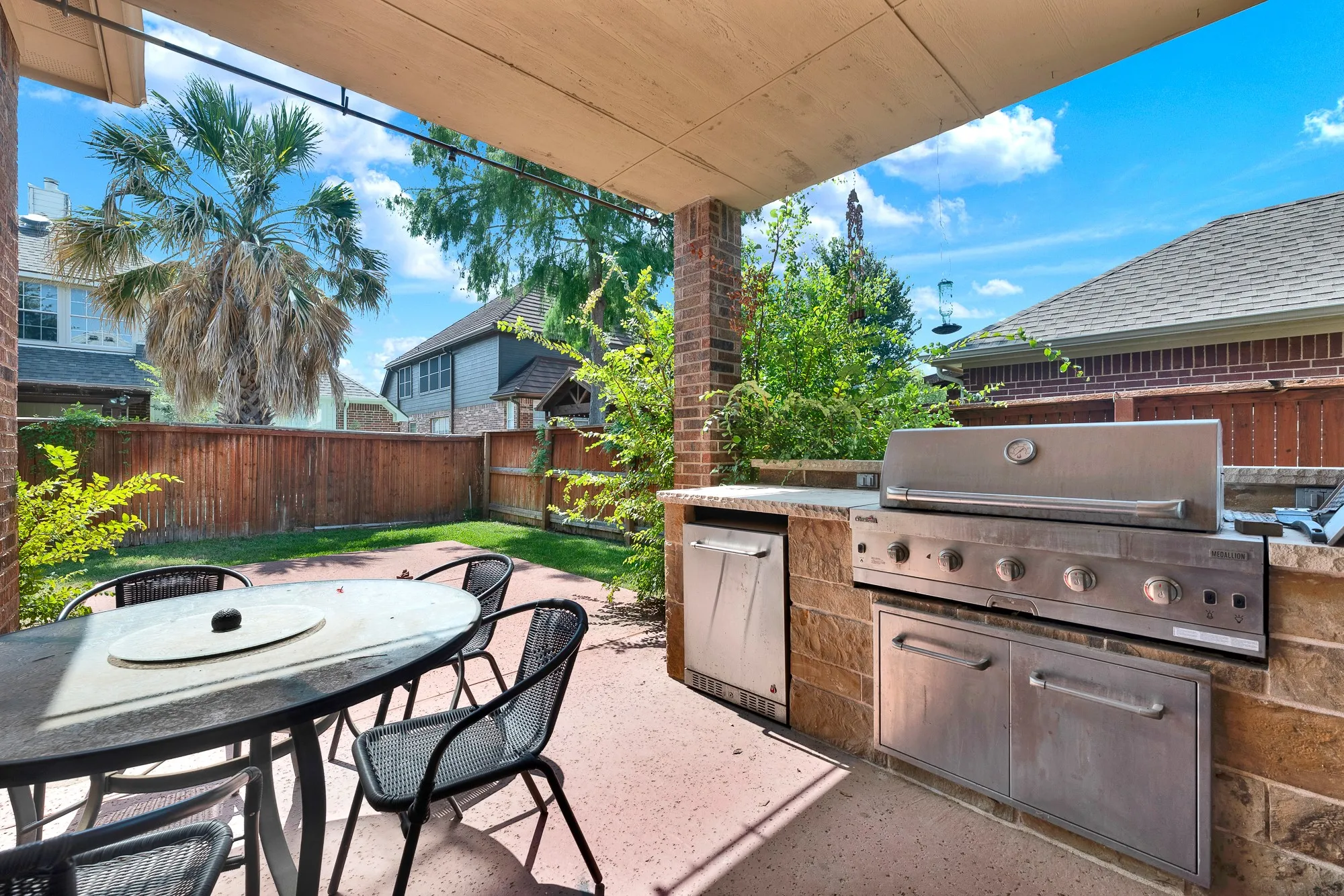 Covered patio with an outdoor kitchen featuring a built-in grill, integrated stainless steel cabinetry, and brick-clad base