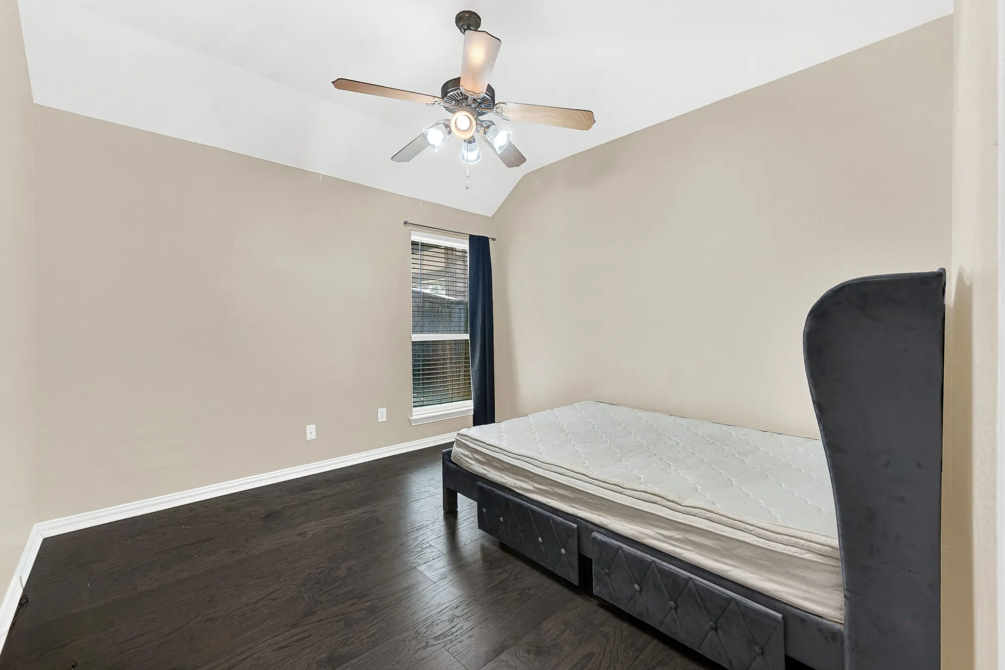 Vaulted ceiling with a ceiling fan, dark wood-finish flooring, and a window with blinds and drapes