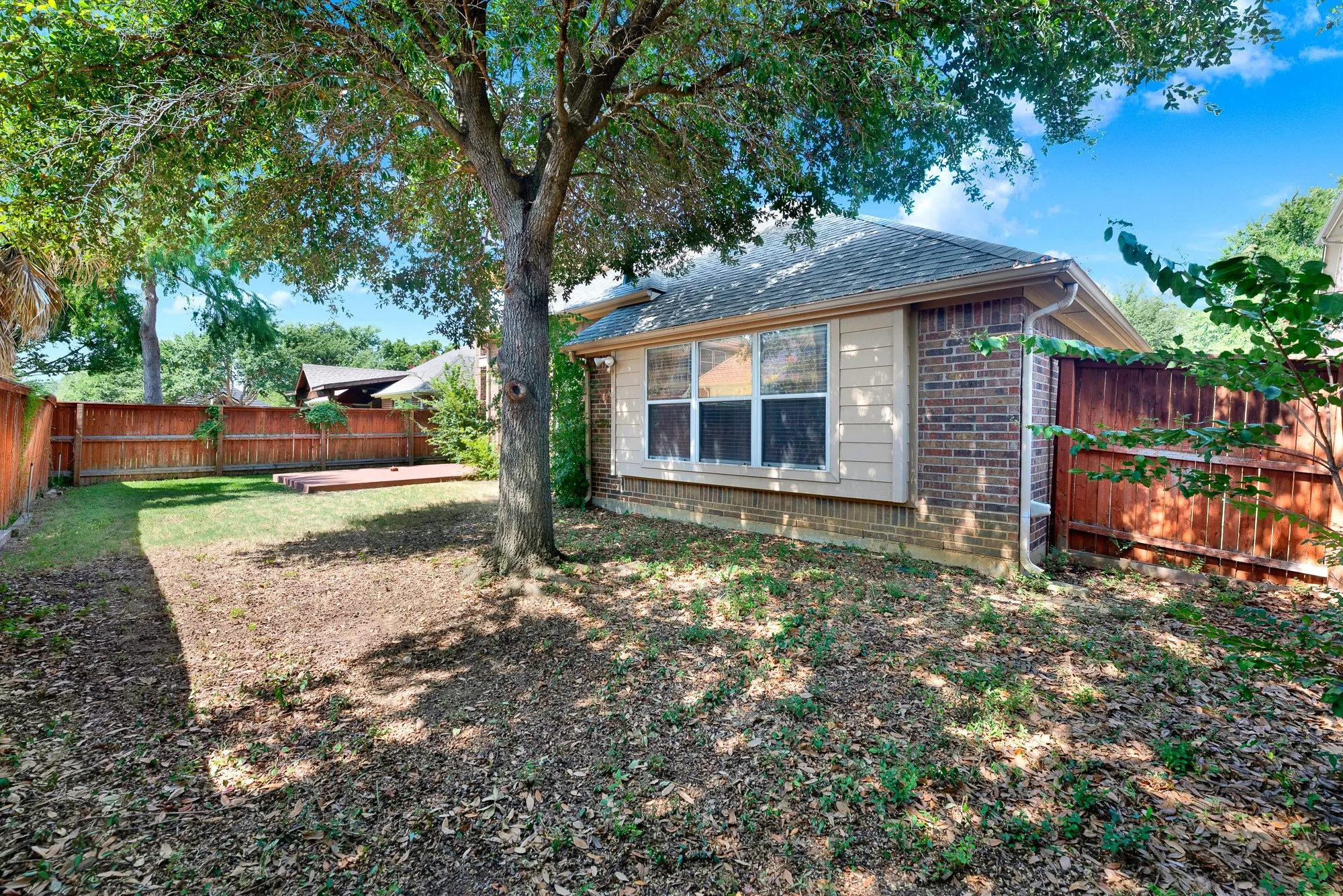 Expansive backyard featuring a manicured lawn, mature shade tree, privacy fencing, and a built-in wood deck