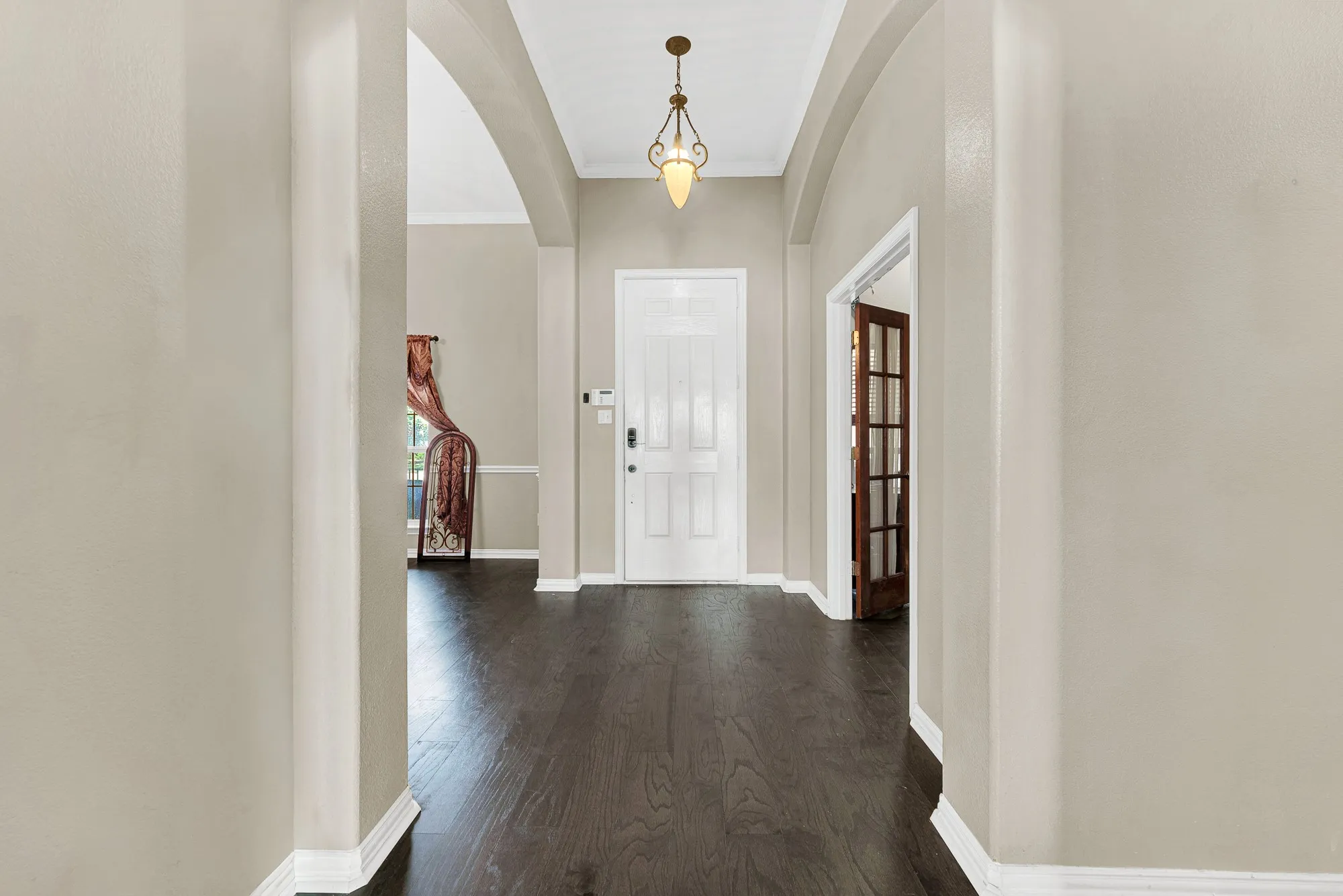 Arched hallway with dark wood-finish flooring, a decorative pendant light, and a white paneled entry door