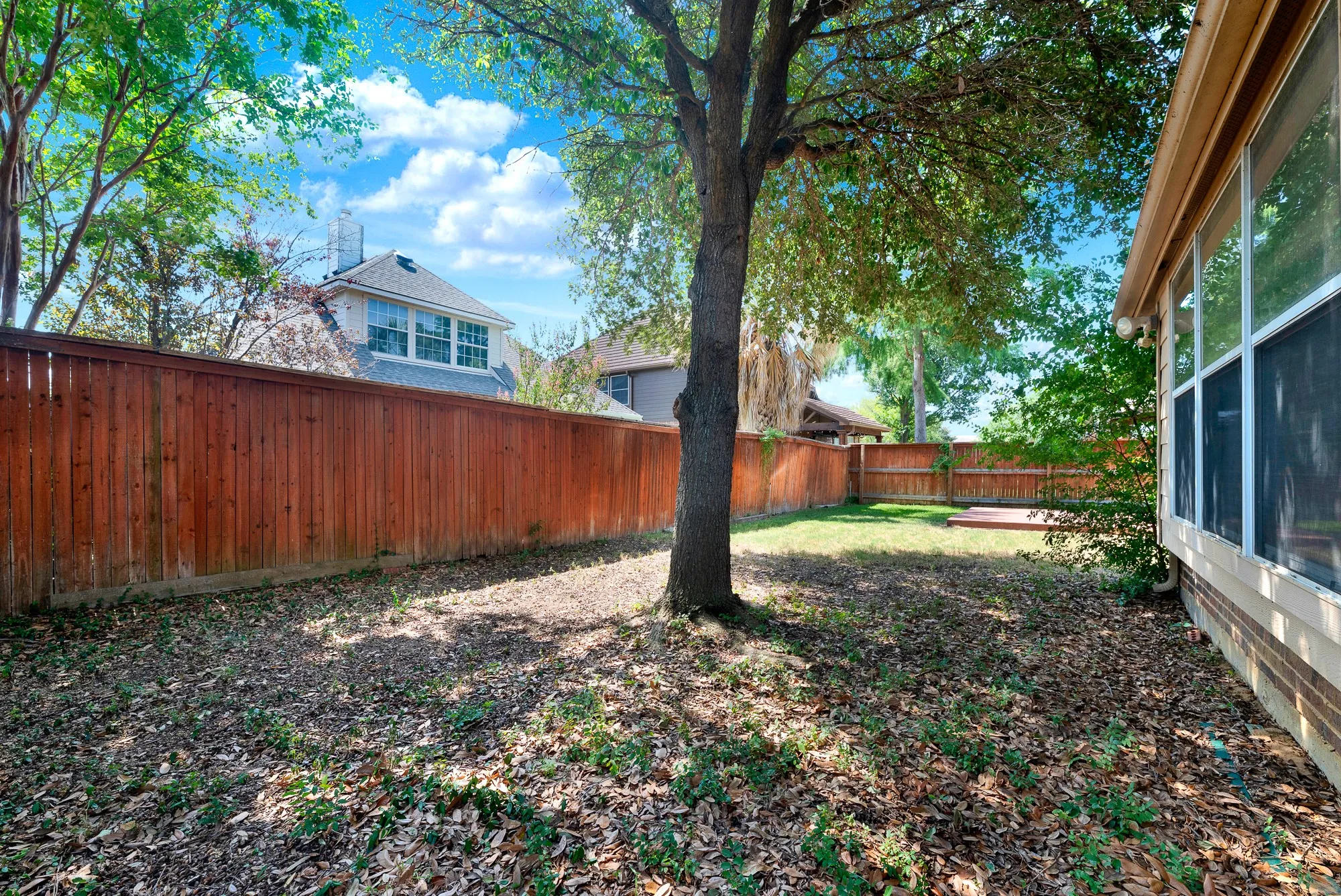 Expansive backyard featuring a mature tree, privacy fencing, and a sunroom exterior with multiple windows