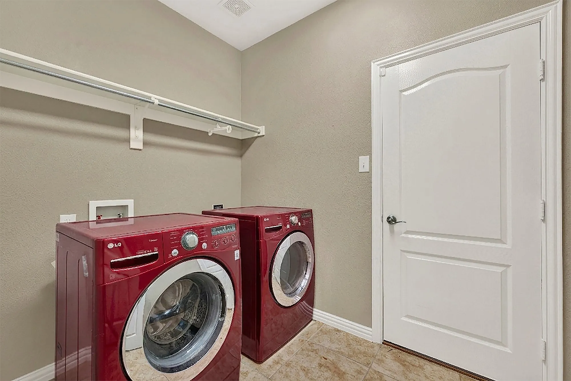 Laundry area featuring a built-in hanging rod, textured walls, and tile flooring