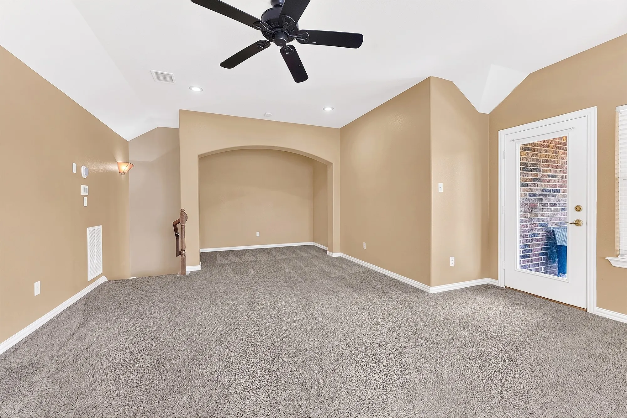 Spacious room featuring vaulted ceilings, a ceiling fan, recessed lighting, an arched alcove, and a glass-paneled door