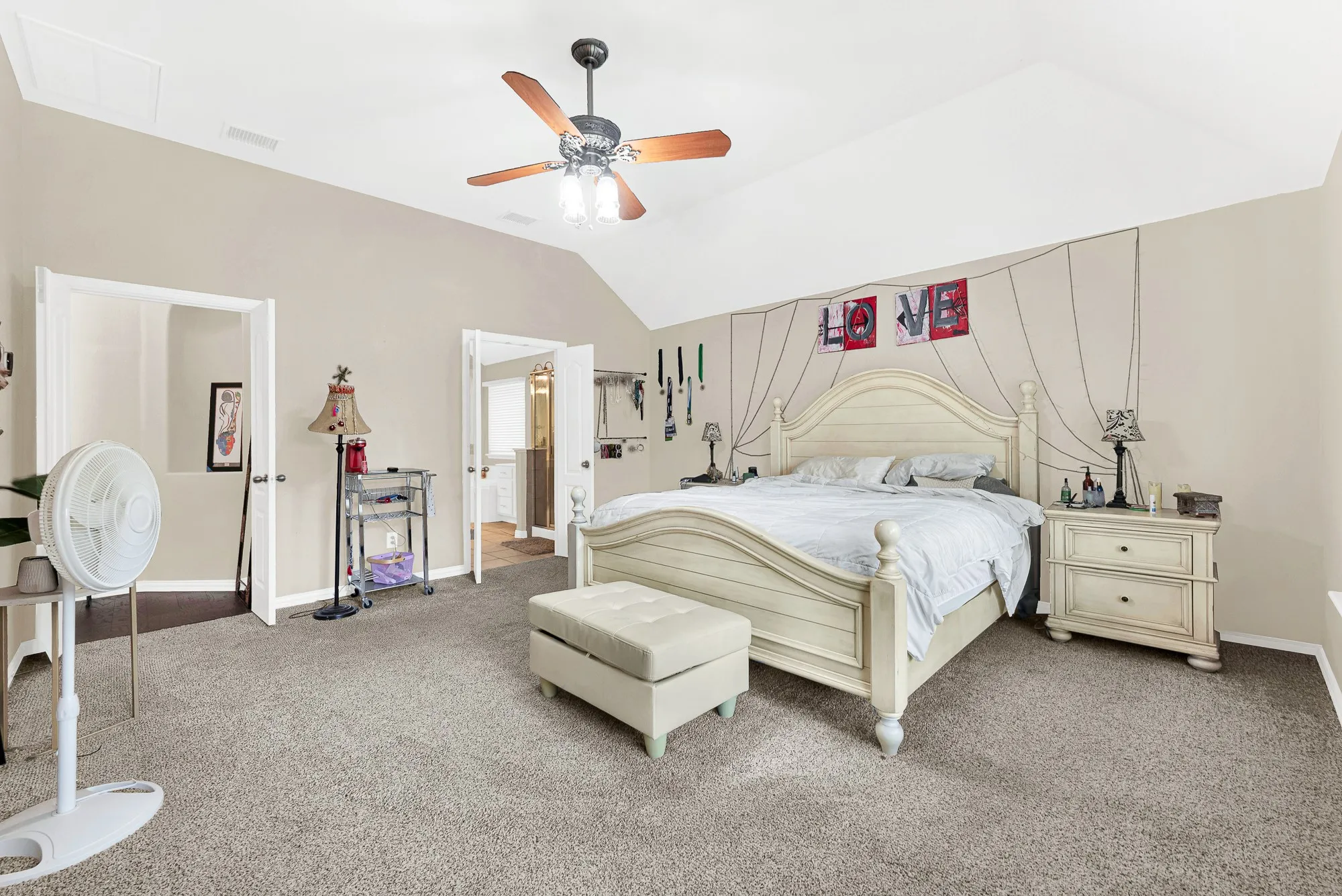 Vaulted ceiling with a ceiling fan, neutral carpeting, and a doorway opening to an additional space