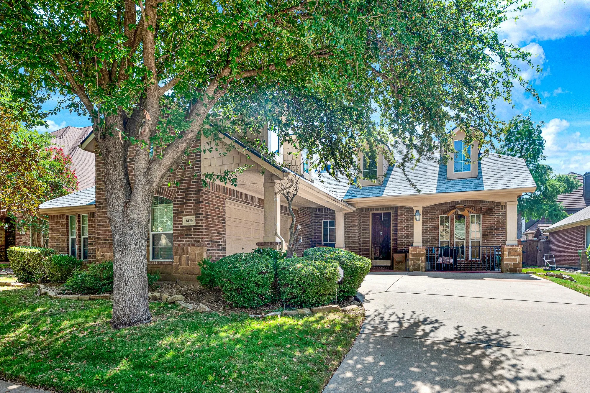 Brick and stone facade, dormer windows, covered entry, attached garage, and a concrete driveway