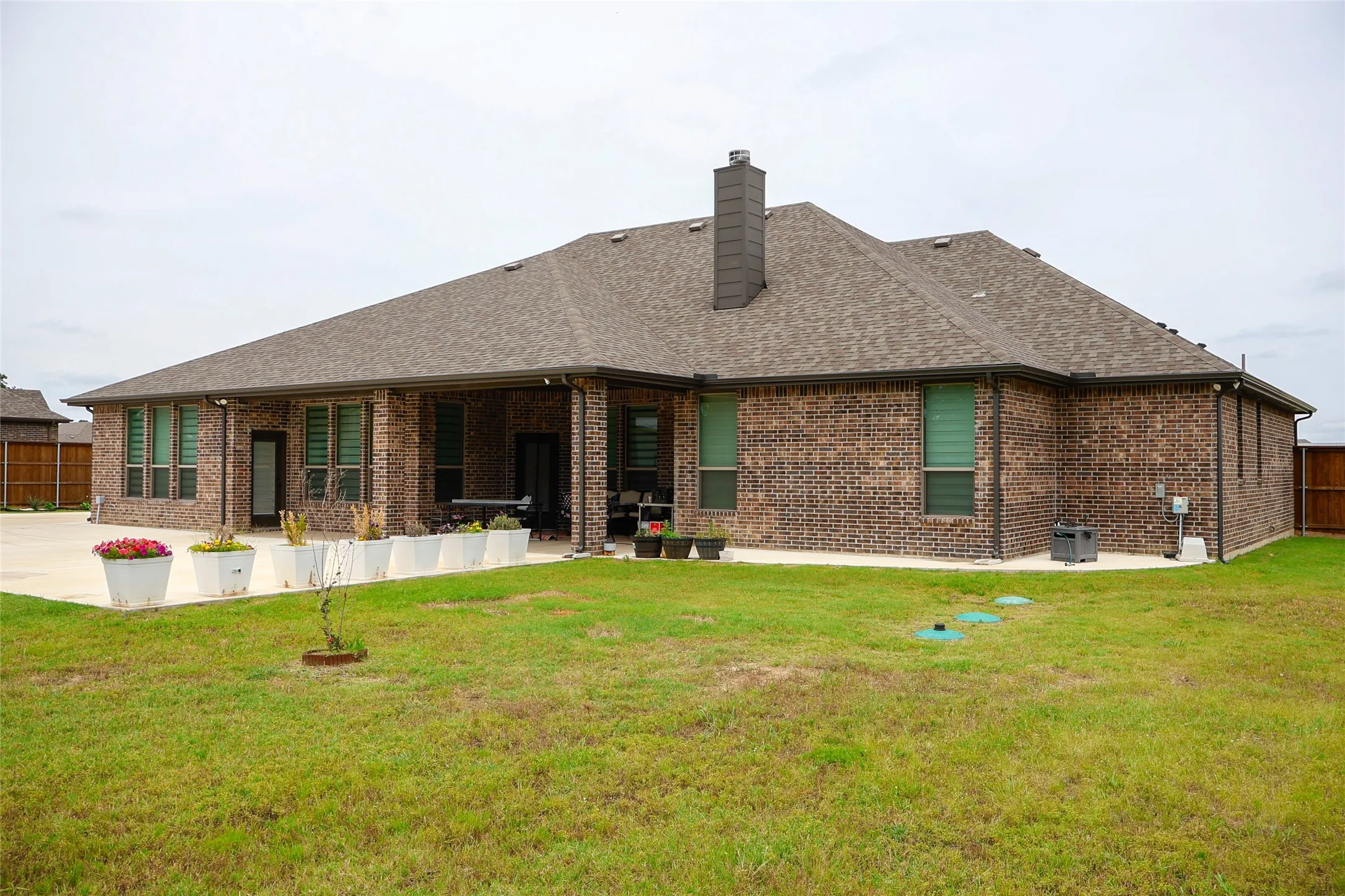 Brick exterior featuring a covered patio, multiple windows with blinds, and a brown shingle roof