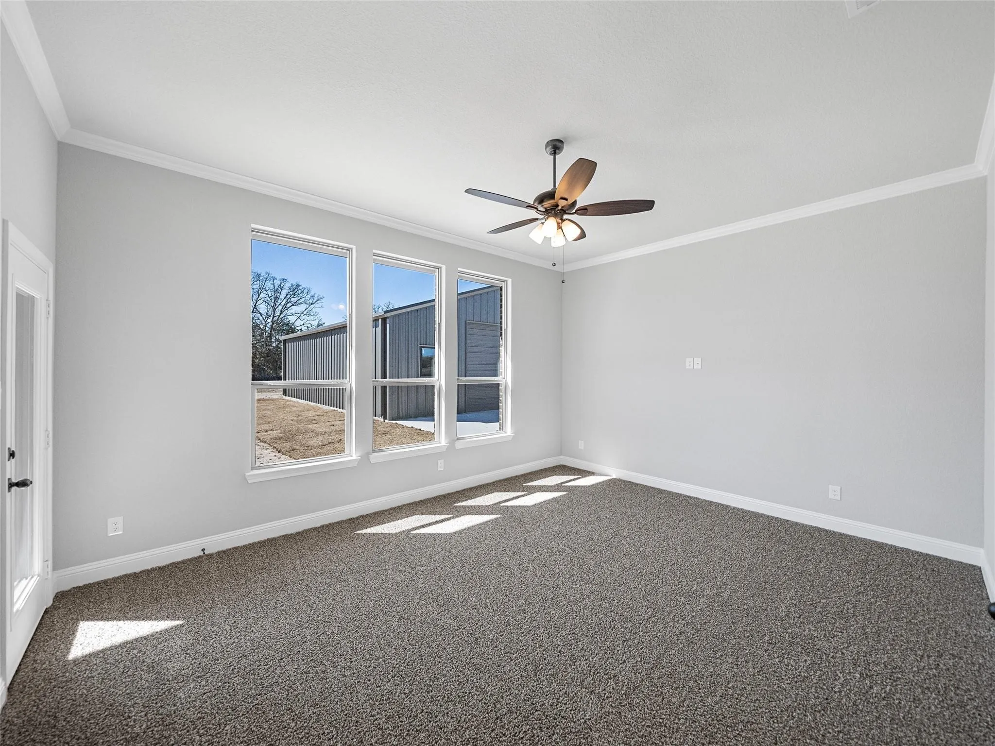 Spacious room featuring three large windows, crown molding, a ceiling fan with integrated lighting, and neutral-toned carpeting
