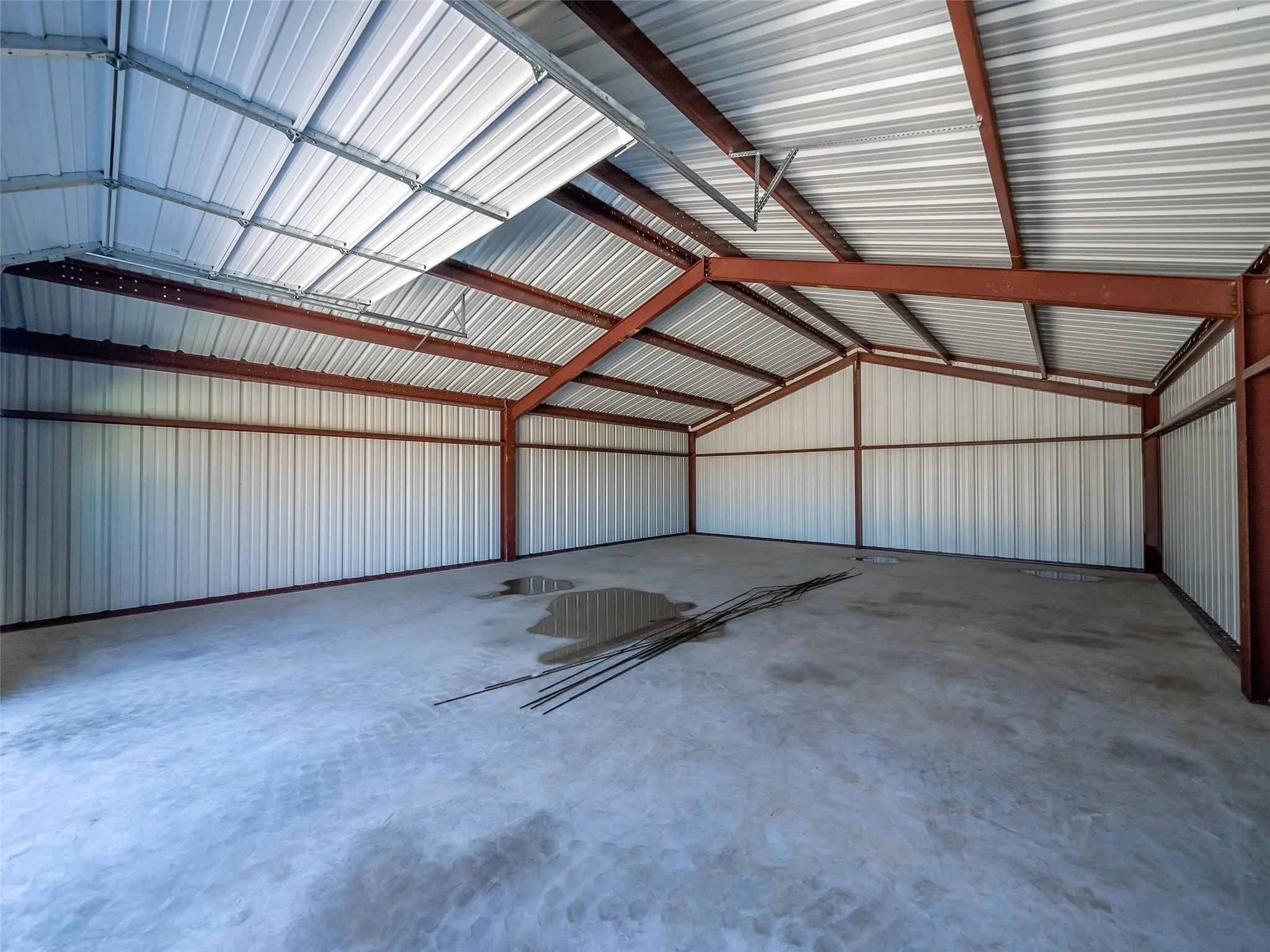 Spacious metal building featuring a vaulted ceiling with exposed steel beams, corrugated metal walls, and a concrete floor
