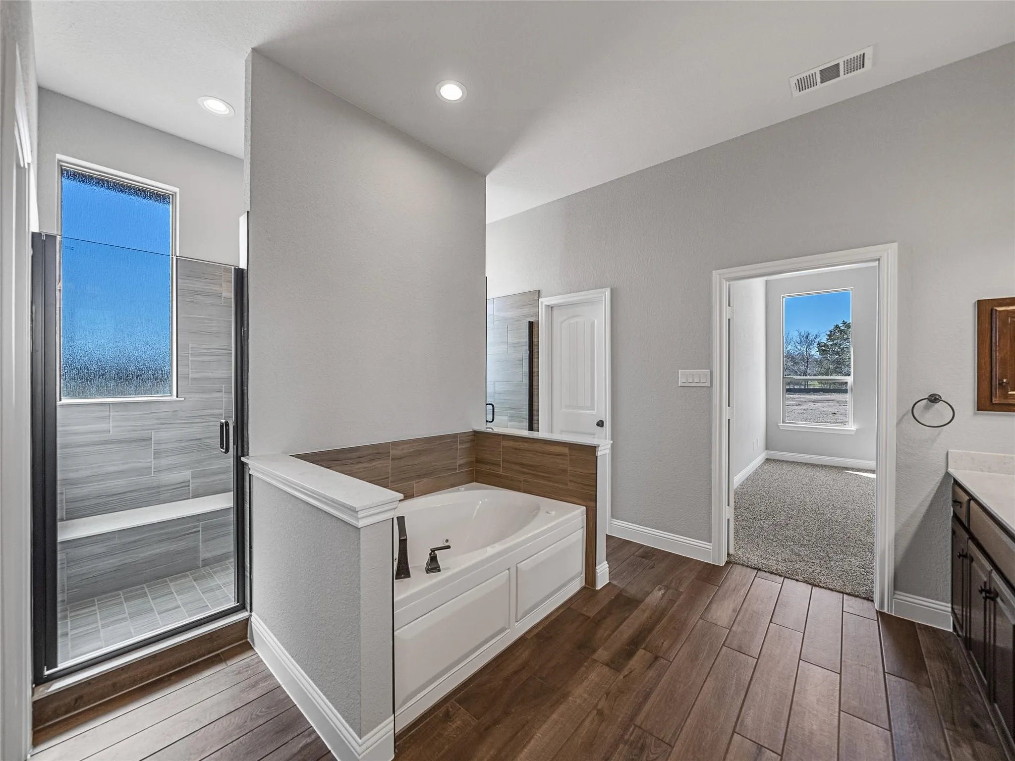 Bathroom featuring a built-in soaking tub with a tiled surround, a glass-enclosed shower with a bench, wood-finish tile flooring, recessed lighting, and a dark wood vanity with a light-toned countertop