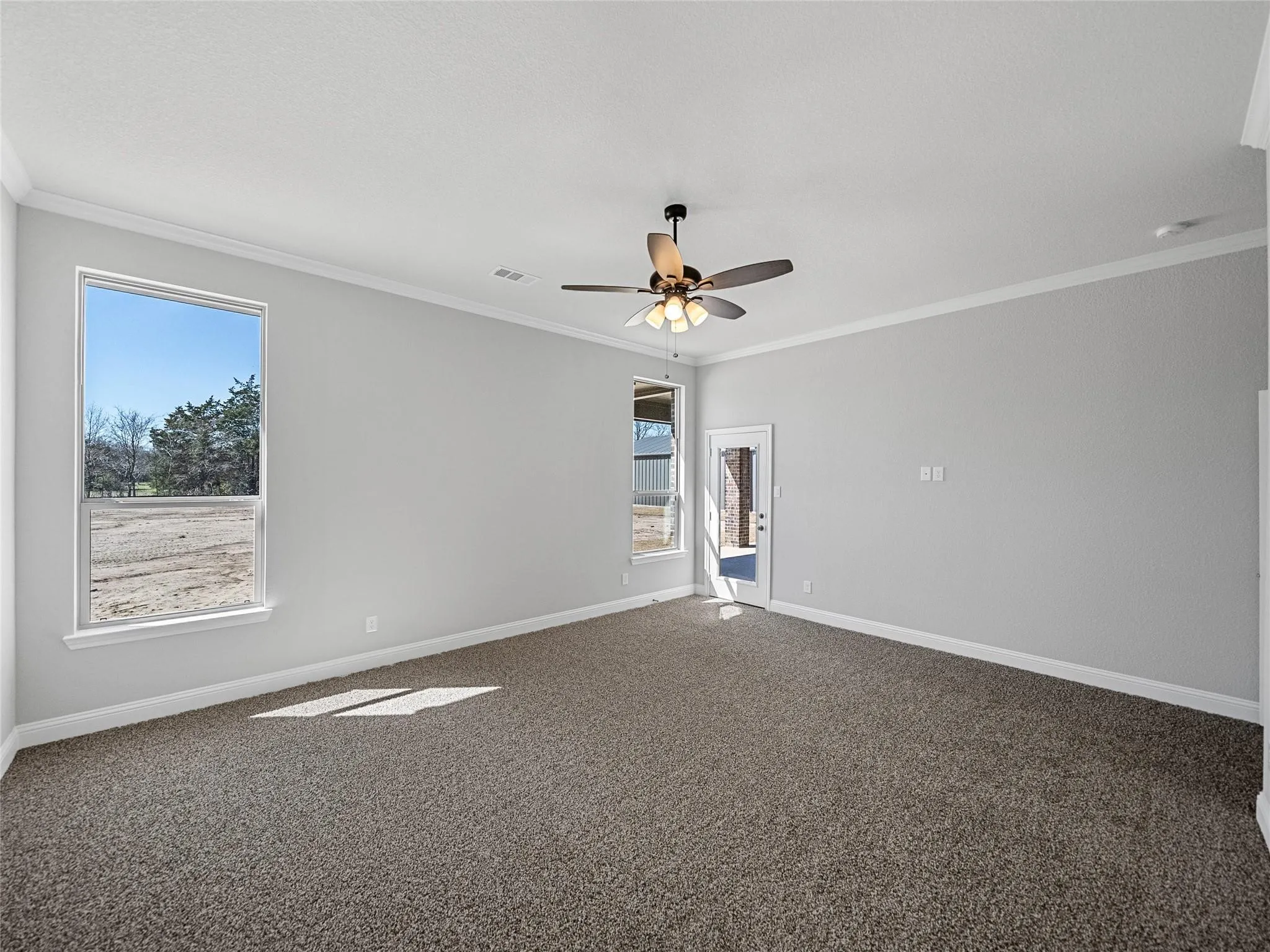 Spacious room featuring light gray walls, textured carpeting, and white crown molding