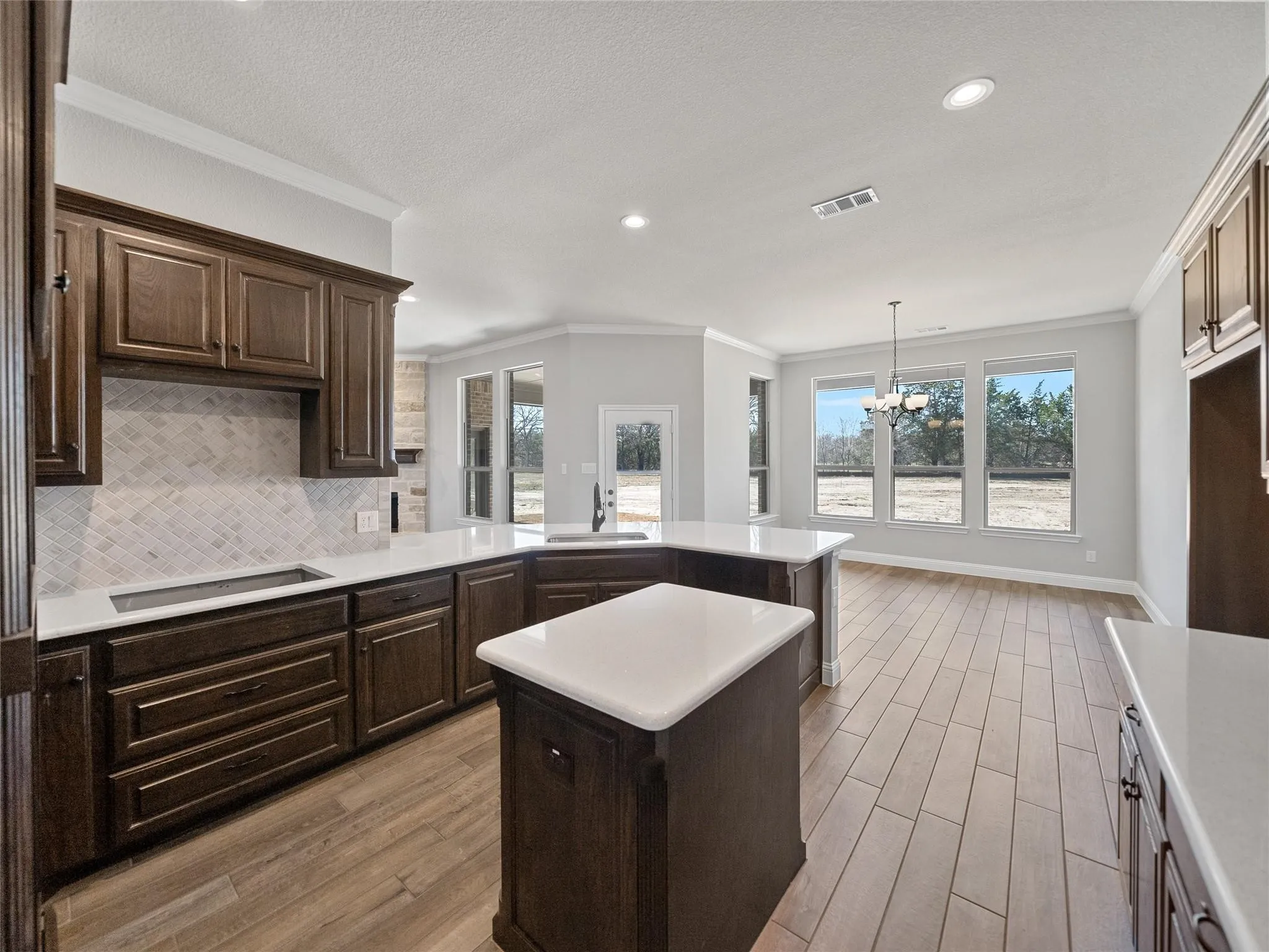 Open-concept kitchen featuring dark wood cabinetry, white countertops, and a subway tile backsplash