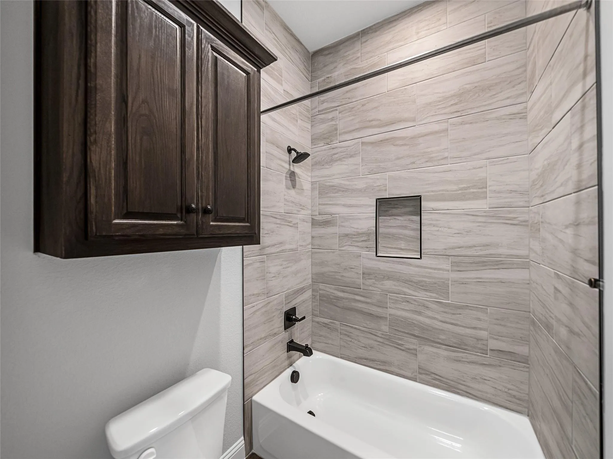 Bathtub with light-toned rectangular wall tiling, featuring a shower niche and matte black fixtures