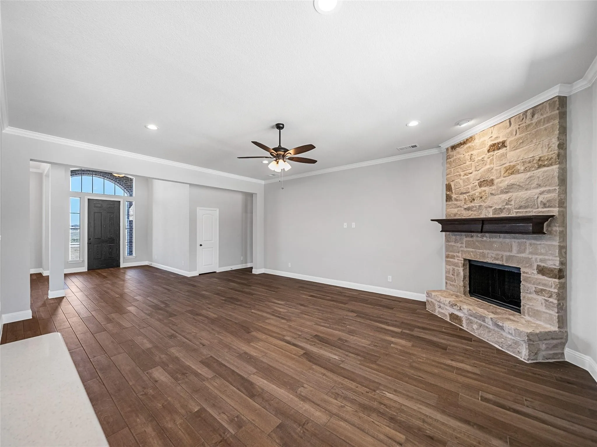 Spacious living area featuring wood-finish flooring, a stone-clad fireplace with a wood mantle, and a ceiling fan