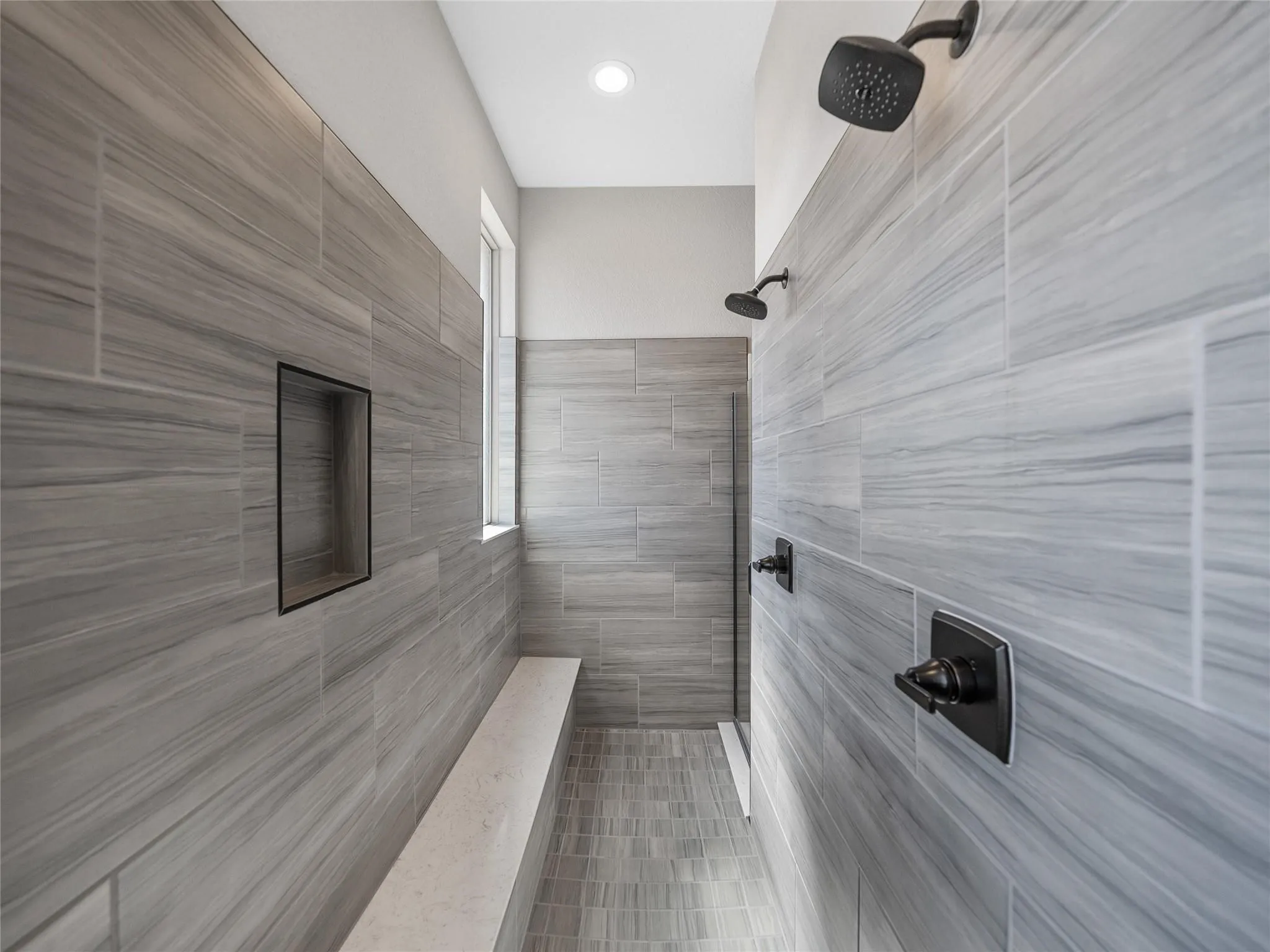 Tiled shower featuring a built-in bench, recessed niche, transom window, and matte black fixtures