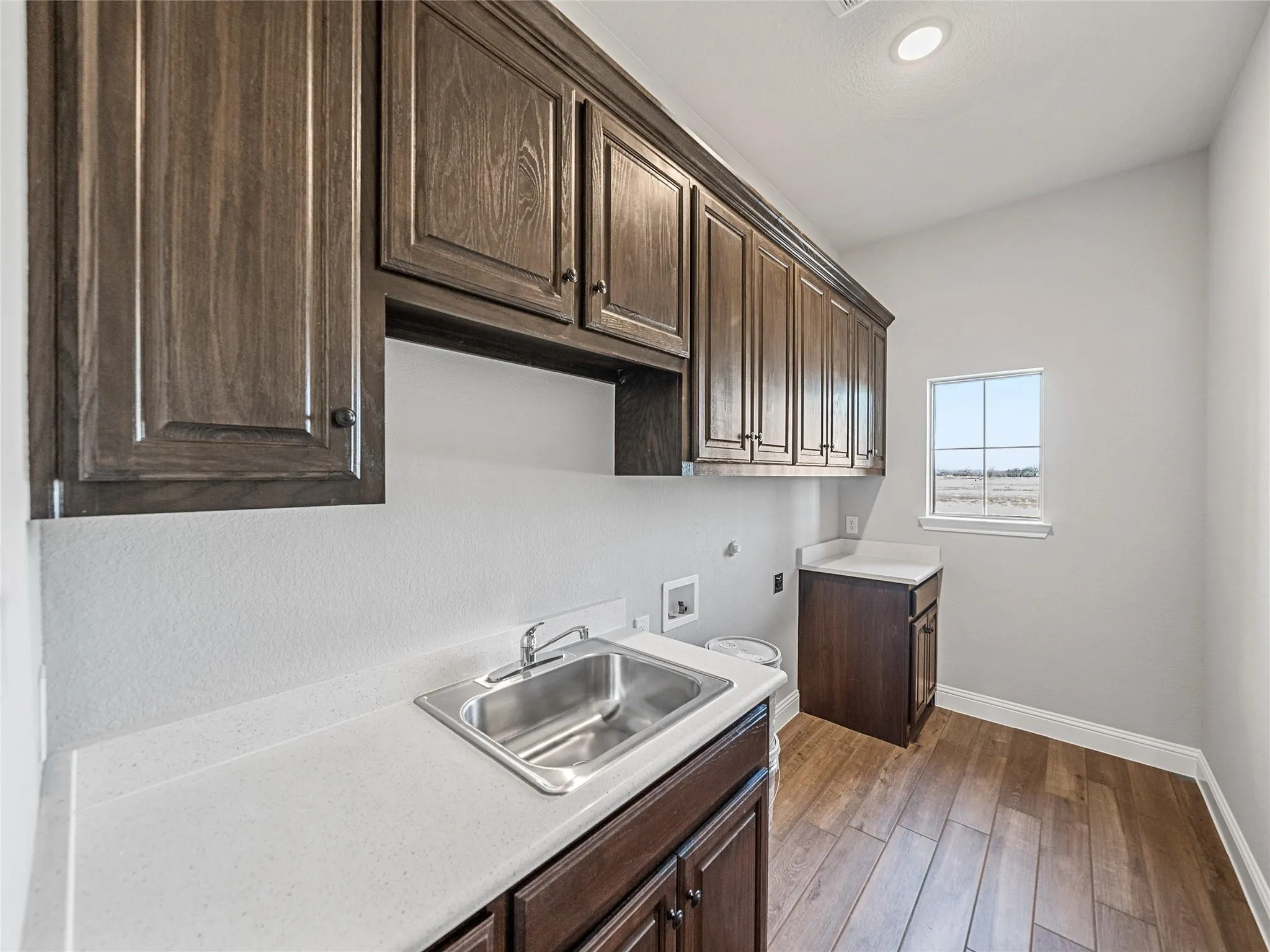 Utility room featuring wood-finish flooring, dark wood cabinetry, light countertops, and a stainless steel sink with a chrome faucet