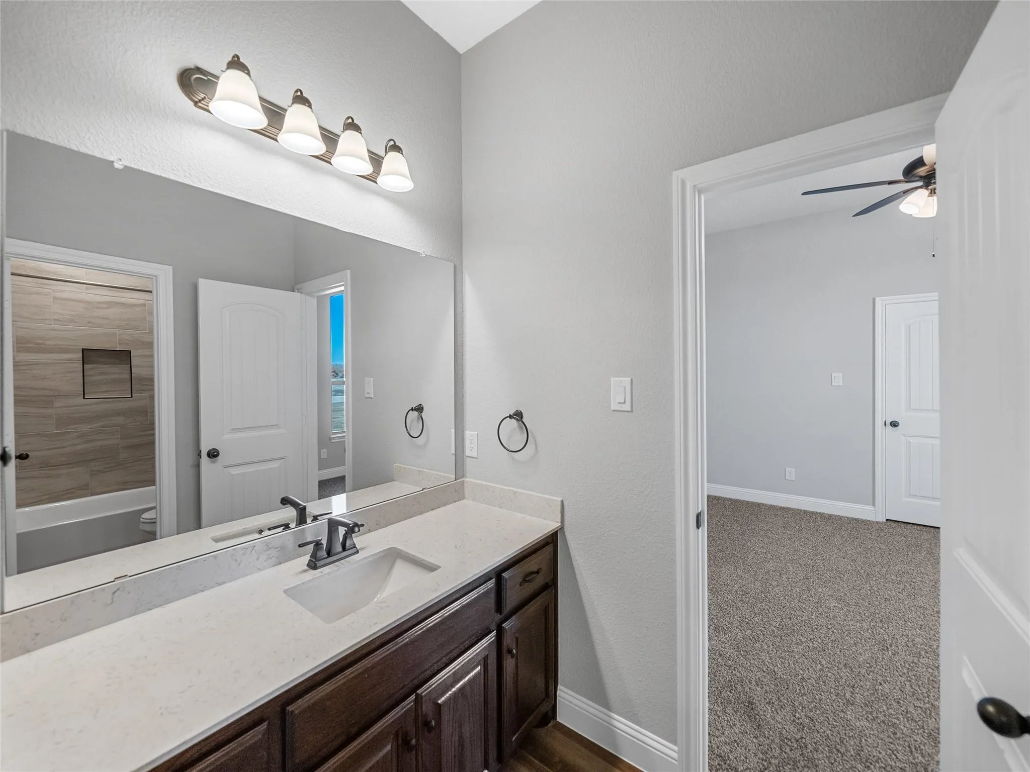 Bathroom vanity featuring a single basin sink set in a light-toned countertop, dark wood-finish cabinetry, and a full-width mirror