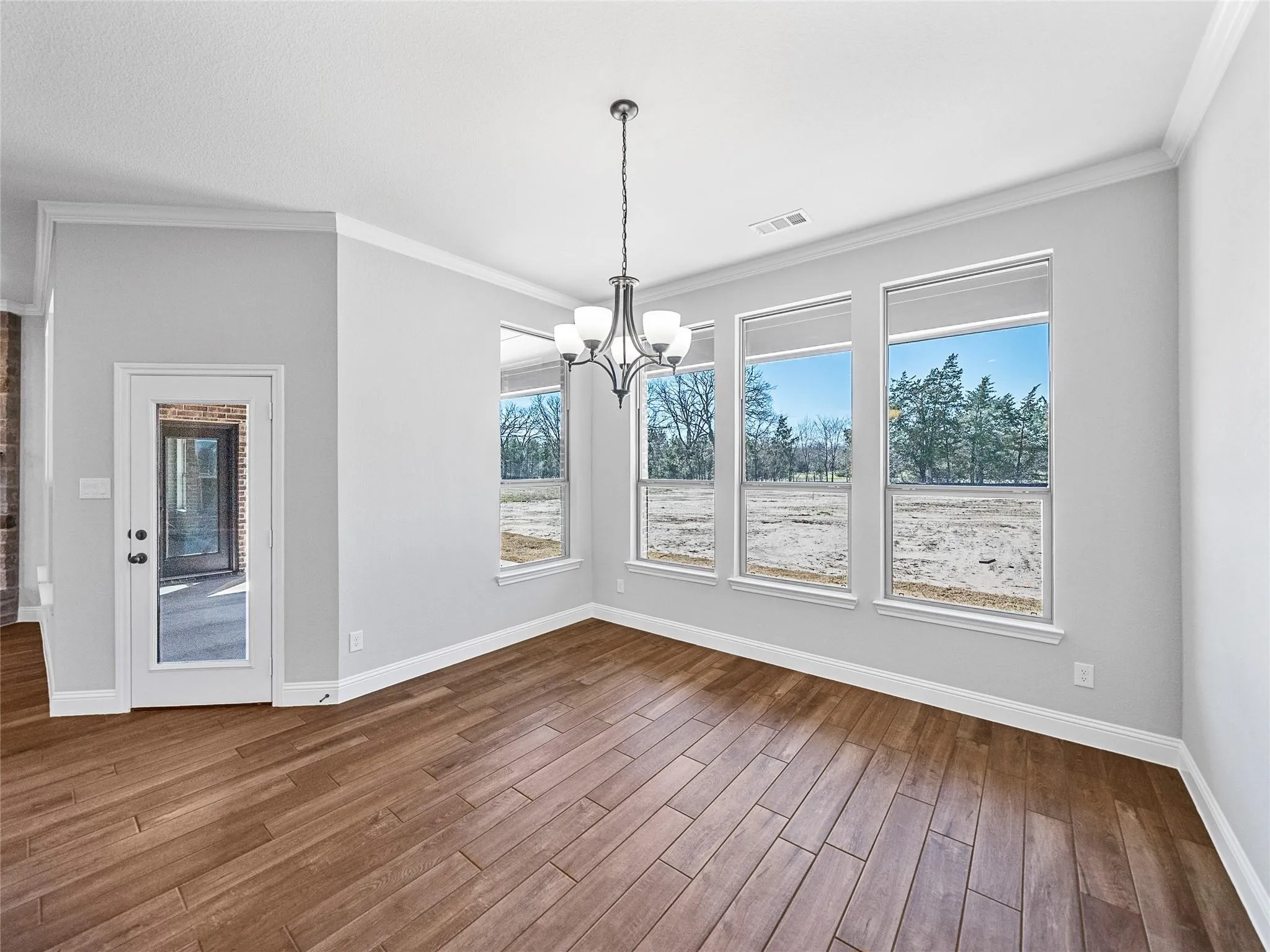 Dining area featuring extensive wood-finish flooring, a contemporary chandelier, and three large windows