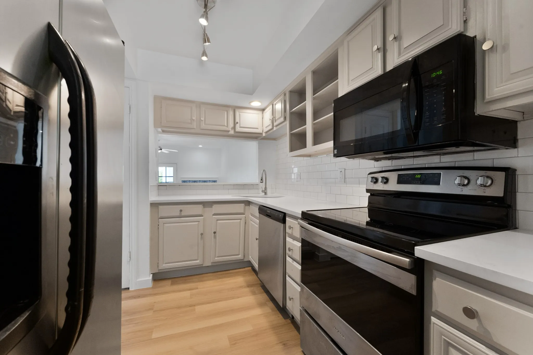 Modern kitchen featuring light-toned cabinetry, stainless steel appliances, a white subway tile backsplash, light countertops, and wood-finish flooring