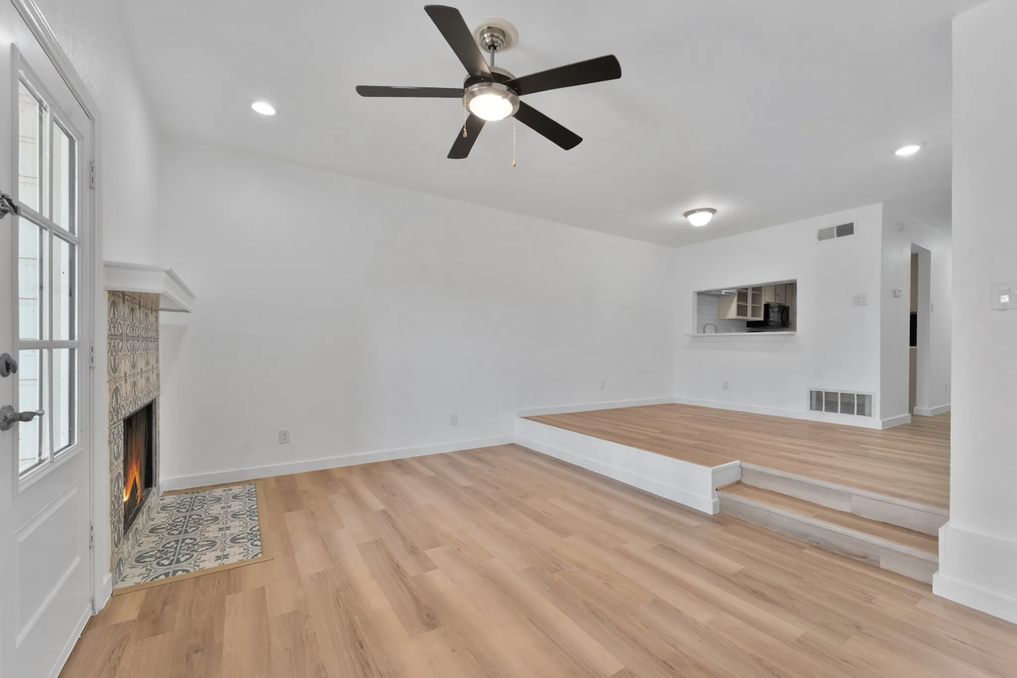 Living area featuring light wood-finish flooring, a tiered floor plan, and a fireplace with decorative tile surround and hearth