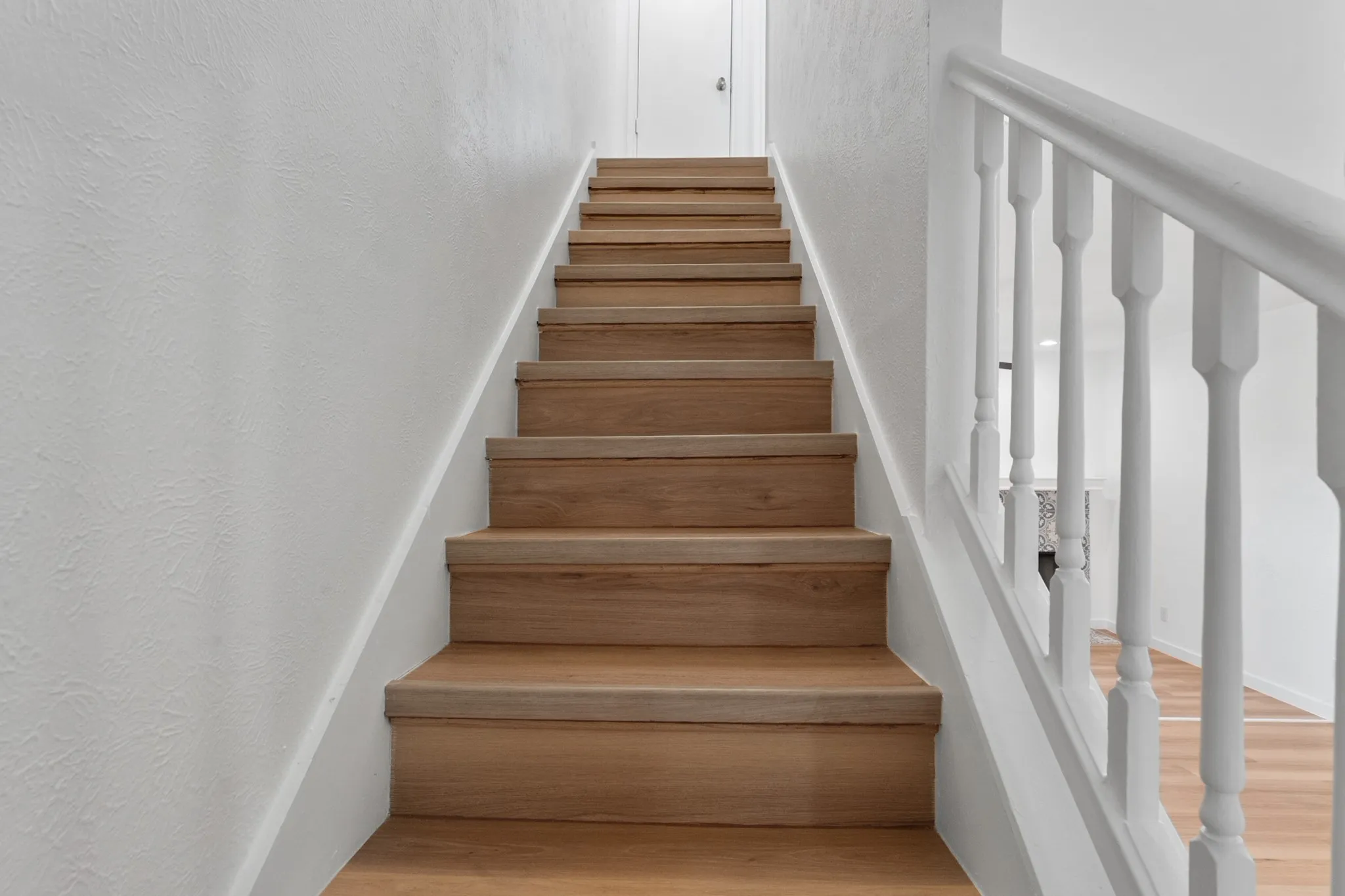 Staircase featuring wood-finish treads and risers, a white painted banister, and white textured walls