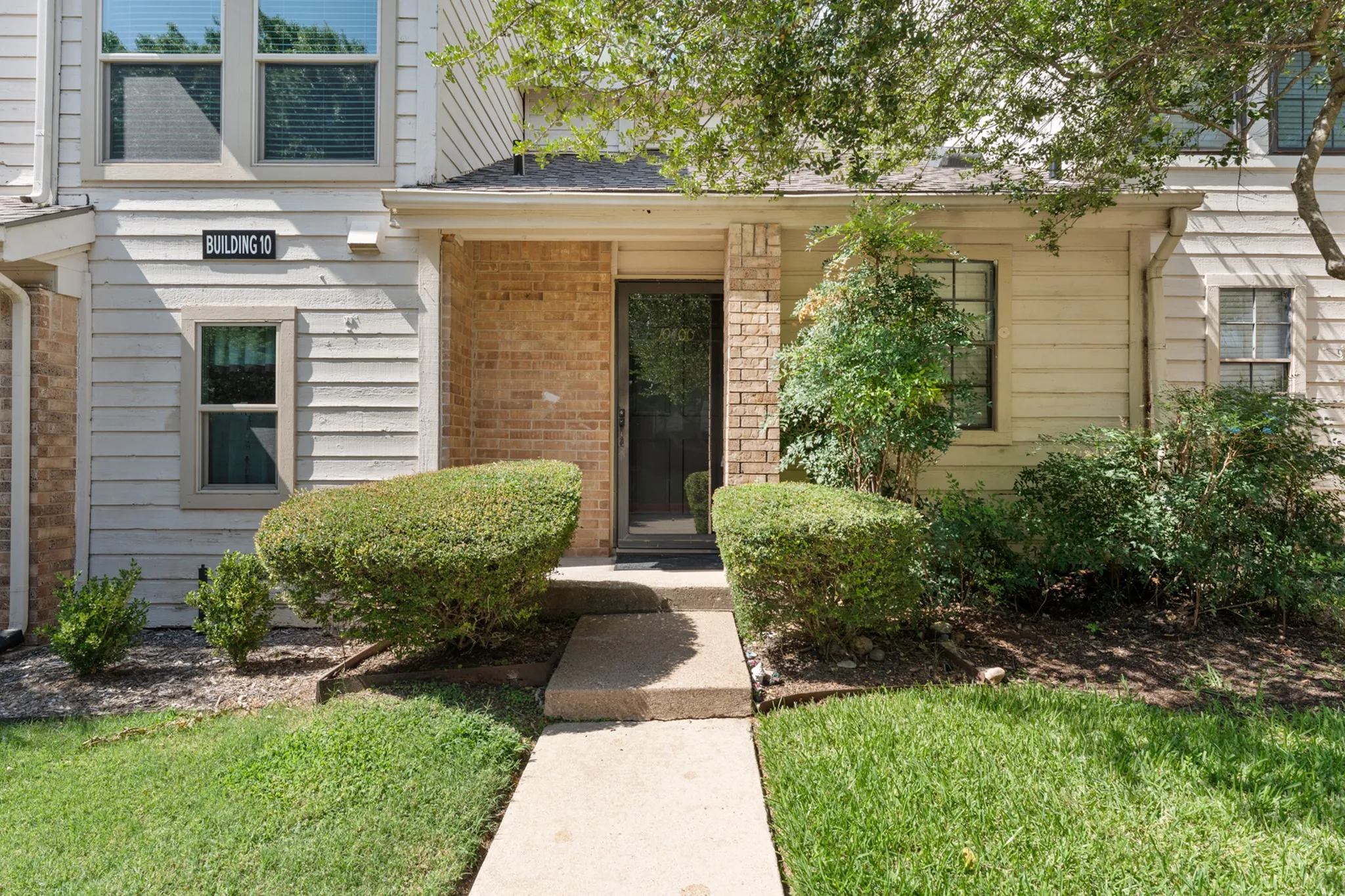 Entryway featuring a concrete walkway, brick accents, exterior siding, and established landscaping