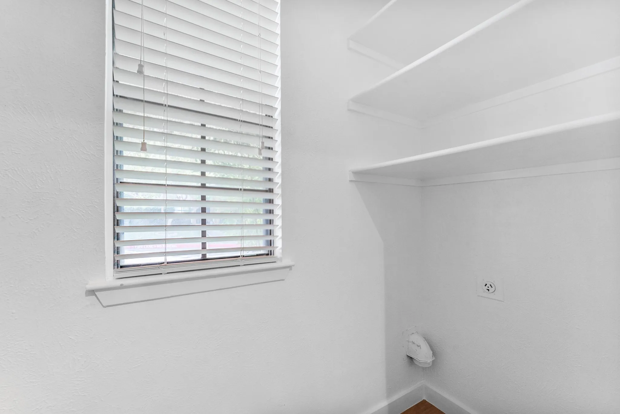 Utility area featuring built-in shelving, a large window with blinds, and white wall finishes