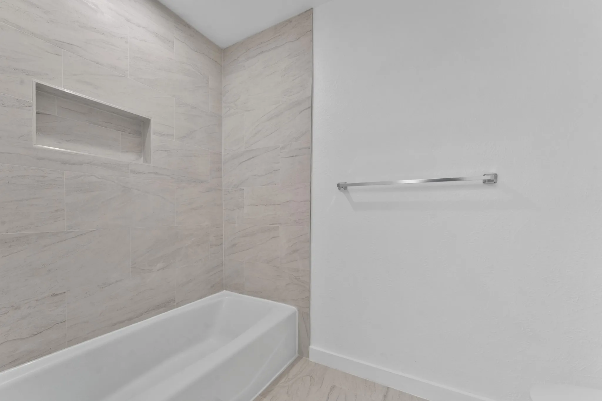 White bathtub with light-colored tile surround featuring a built-in shower niche