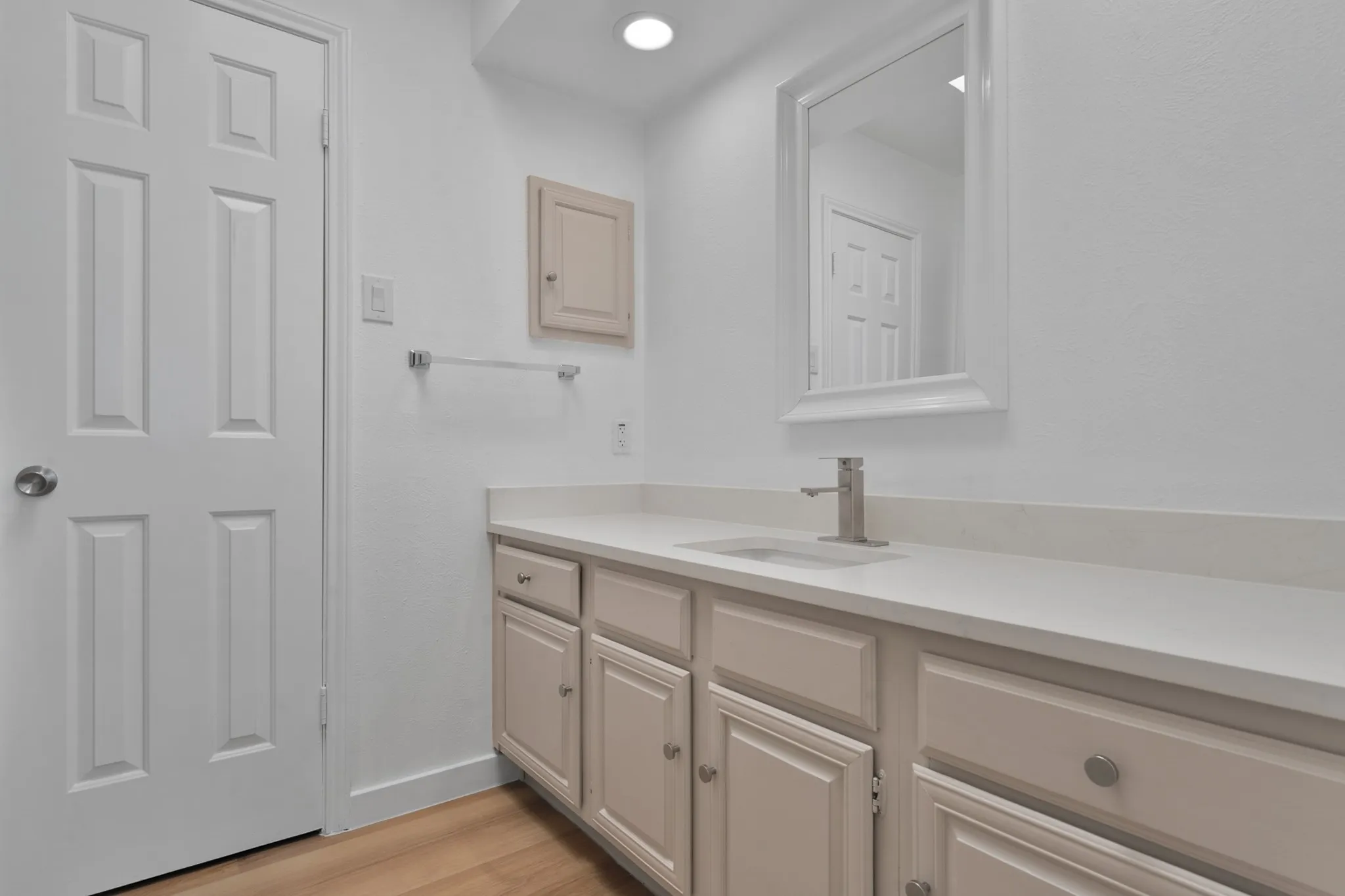 Bathroom vanity featuring light-toned cabinetry with brushed nickel hardware, a white countertop with an integrated sink, and a single-handle faucet