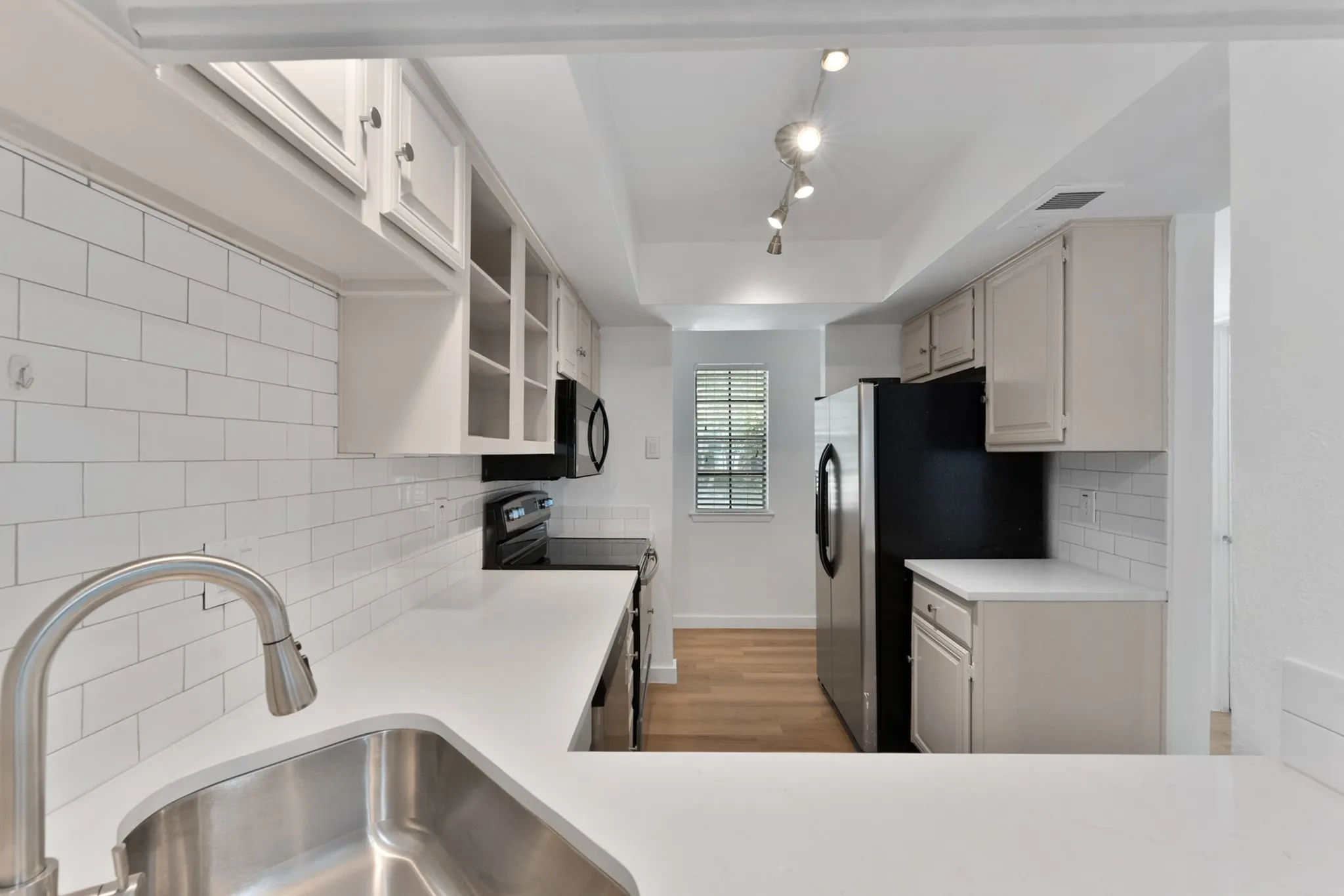 Kitchen featuring white subway tile backsplash, white countertops, stainless steel sink with gooseneck faucet, light-colored cabinetry, and track lighting