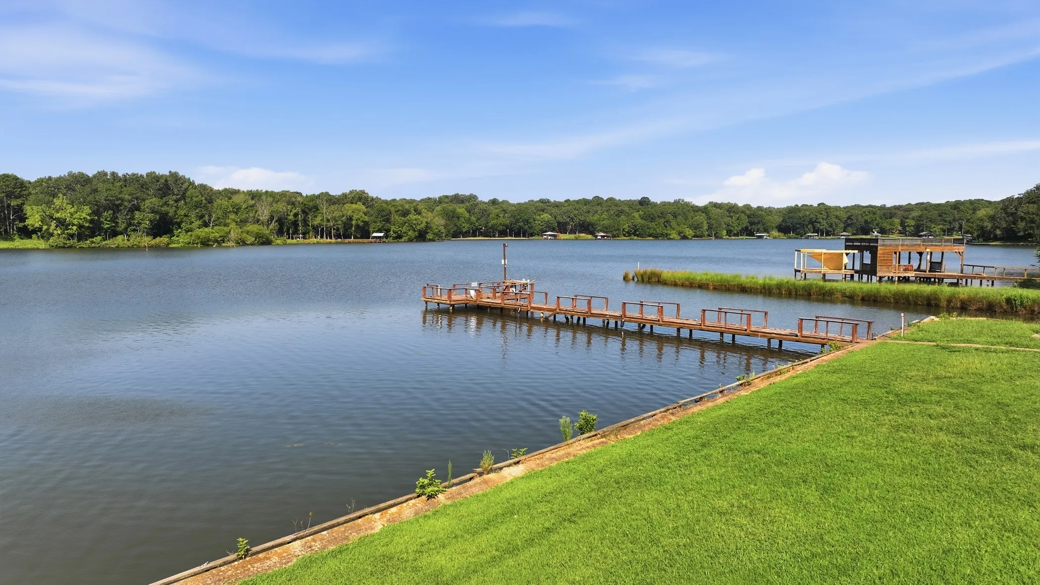 Expansive lakeside property featuring a manicured lawn, a private wooden dock, and a waterfront boathouse with a covered deck