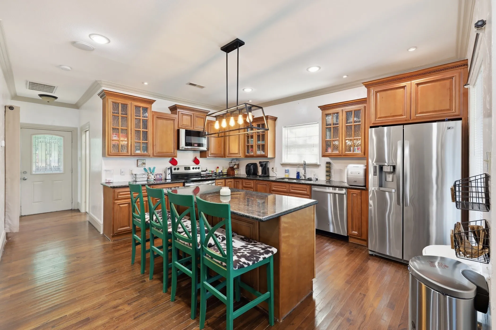 Kitchen featuring warm wood cabinetry, stainless steel appliances, dark stone countertops, and wood-finish flooring
