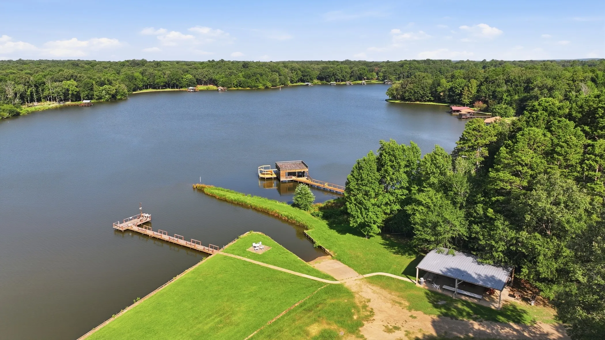 Expansive waterfront property featuring a boat dock, a boat house, a covered pavilion, and a lush green lawn
