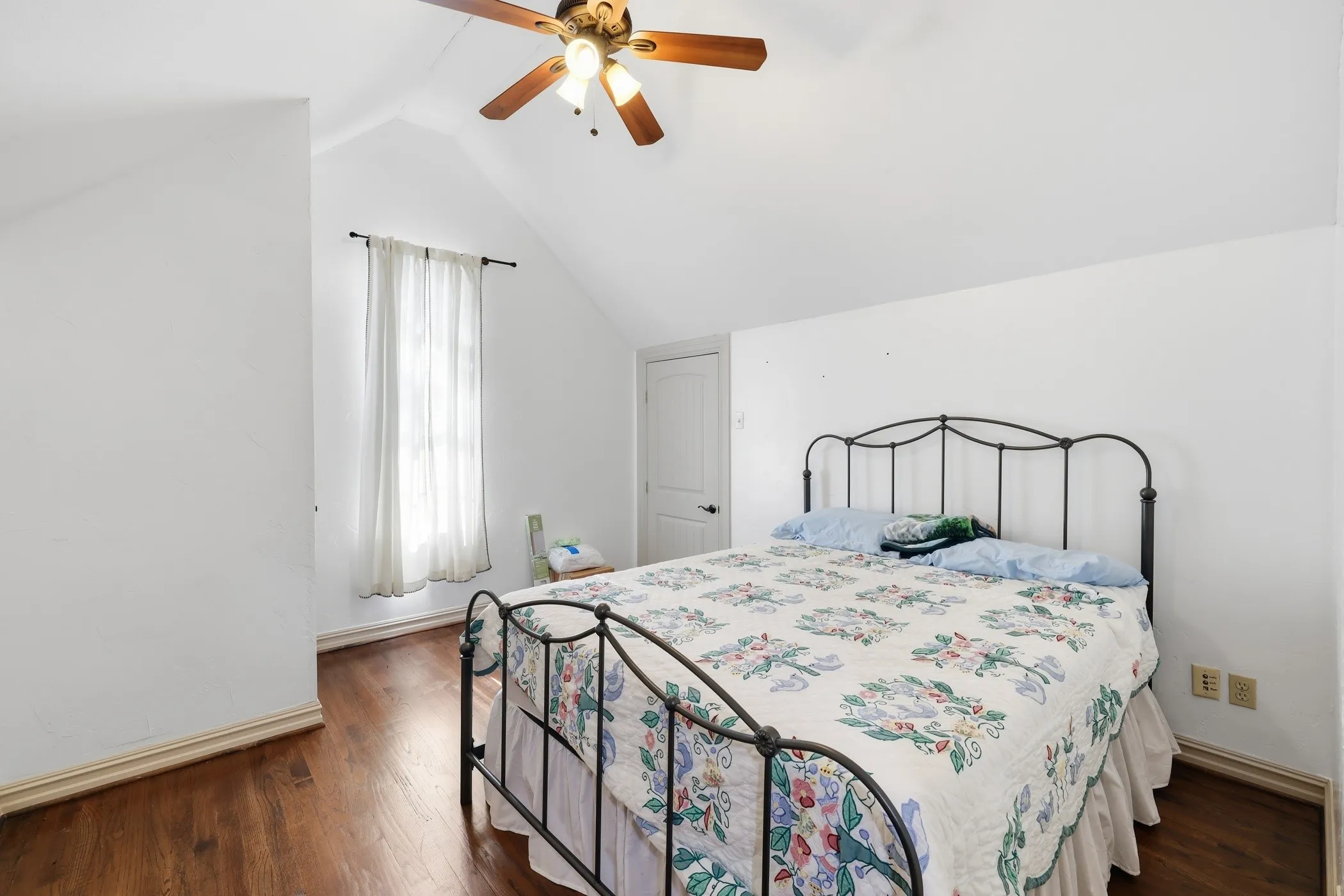 Room featuring vaulted ceilings, wood-finish flooring, a ceiling fan with integrated lighting, and a white interior door