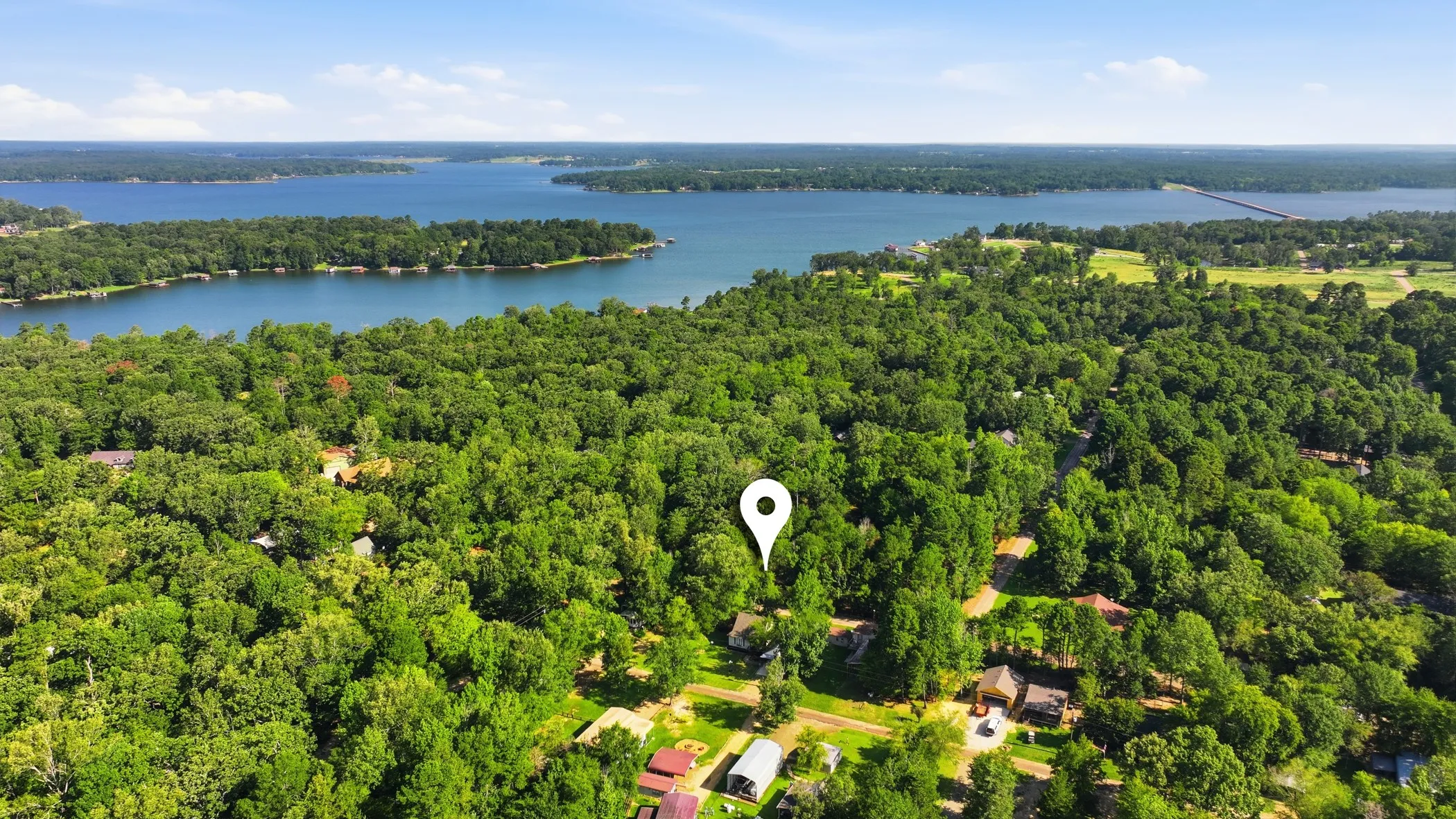 Expansive water body surrounded by lush green tree lines, with scattered residential structures visible through the foliage
