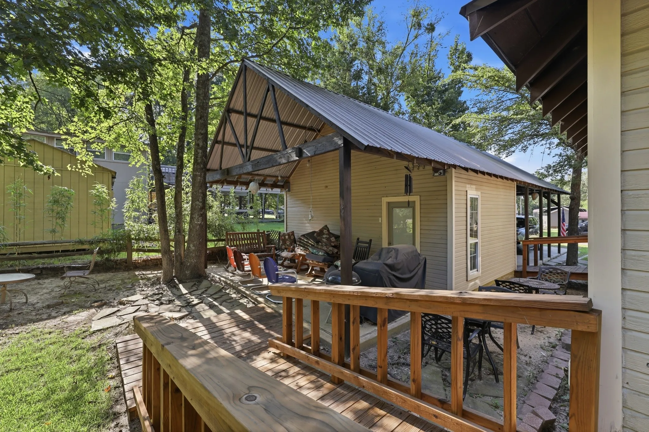 Expansive outdoor area featuring a wood deck, a covered patio with a metal roof, and stone pavers