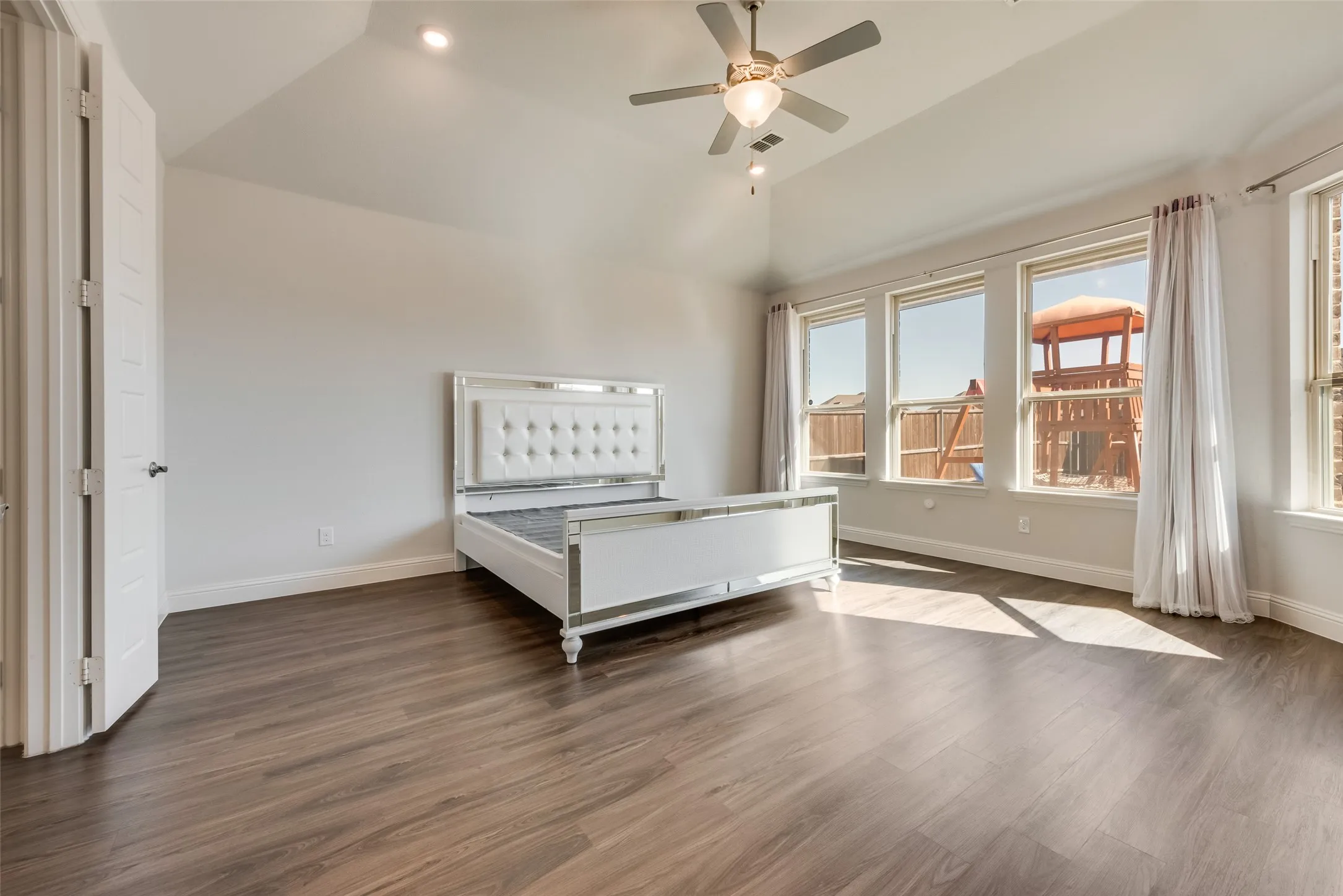Spacious room featuring wood-finish flooring and a vaulted ceiling with a ceiling fan
