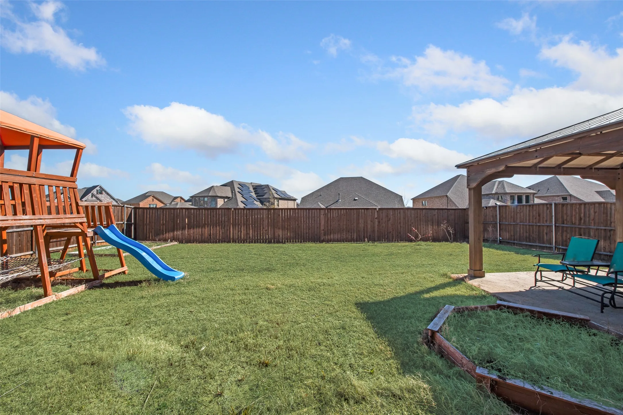 Expansive backyard featuring a manicured lawn, complete privacy fencing, and a covered patio area with a pergola structure