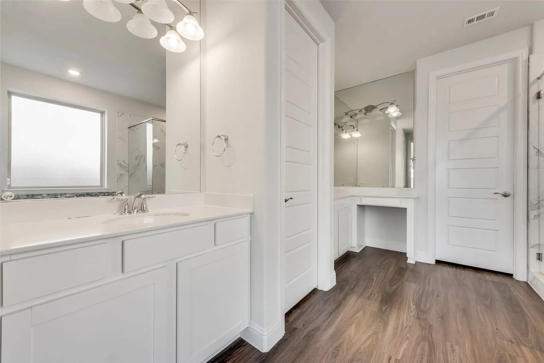 Bathroom featuring wood-finish flooring, white cabinetry, a built-in vanity, a framed mirror, and a window with privacy glass