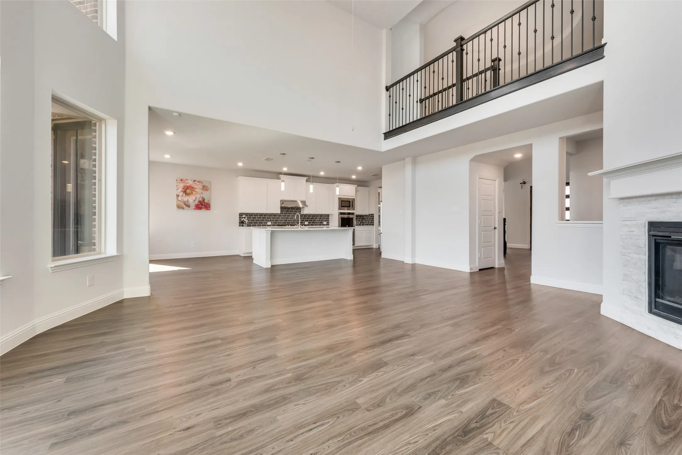 Open-concept living space featuring high ceilings, wood-finish flooring, and a fireplace with a stone surround