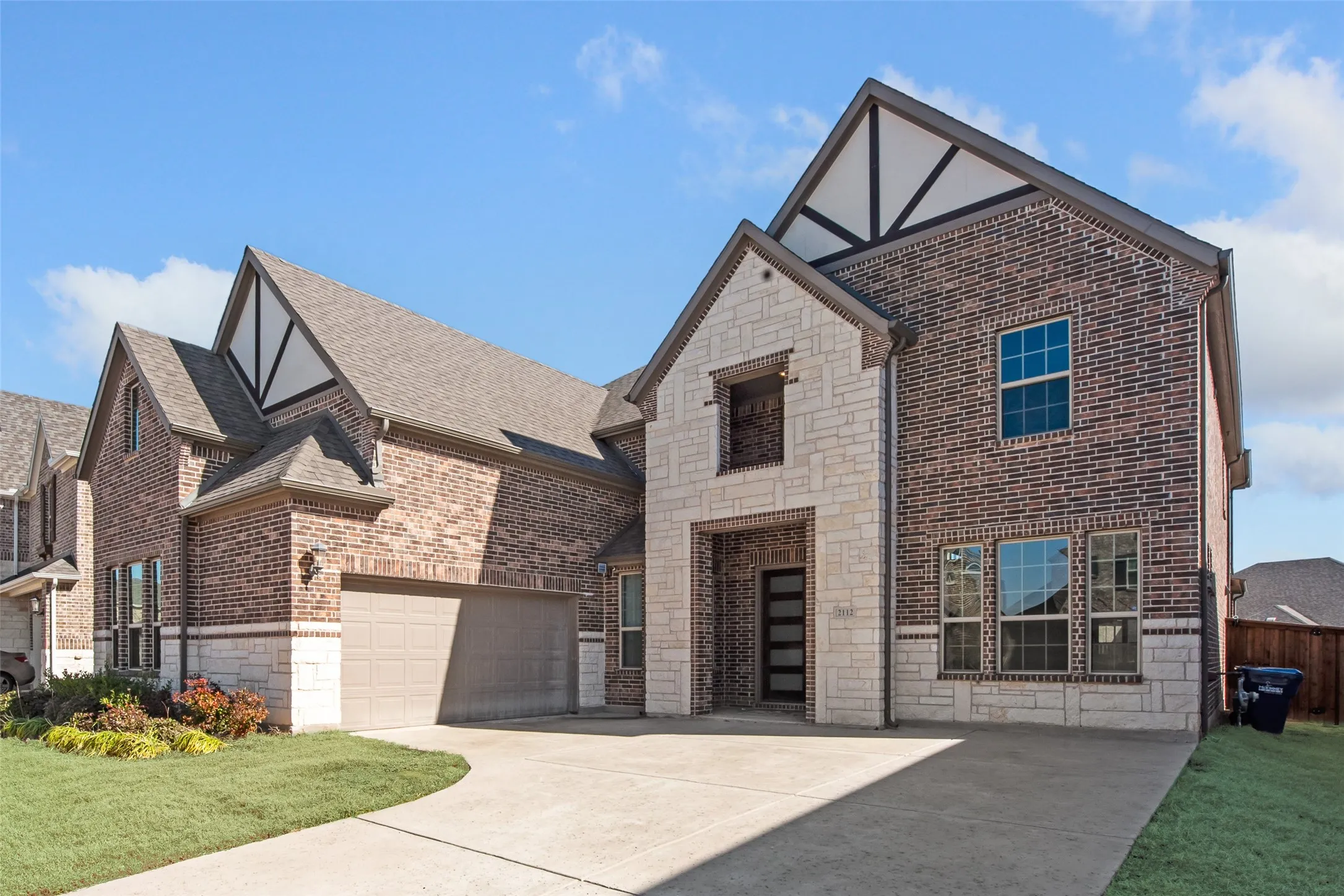 Brick and stone exterior featuring multiple gables, a two-car garage, a covered entry with a modern front door, and a concrete driveway