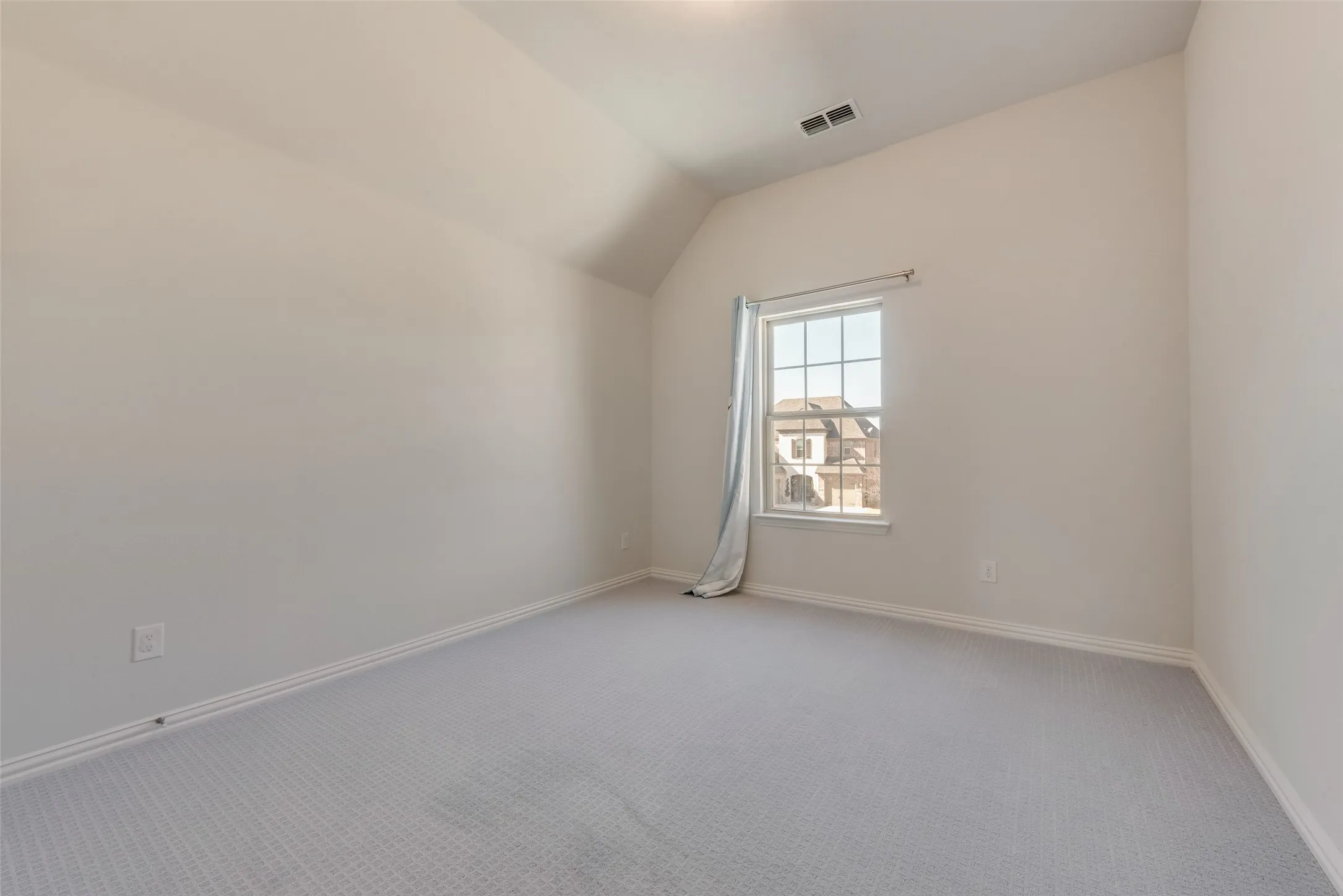 Room featuring a window with grid panes, sloped ceiling, light-colored walls, patterned carpet flooring, and white trim