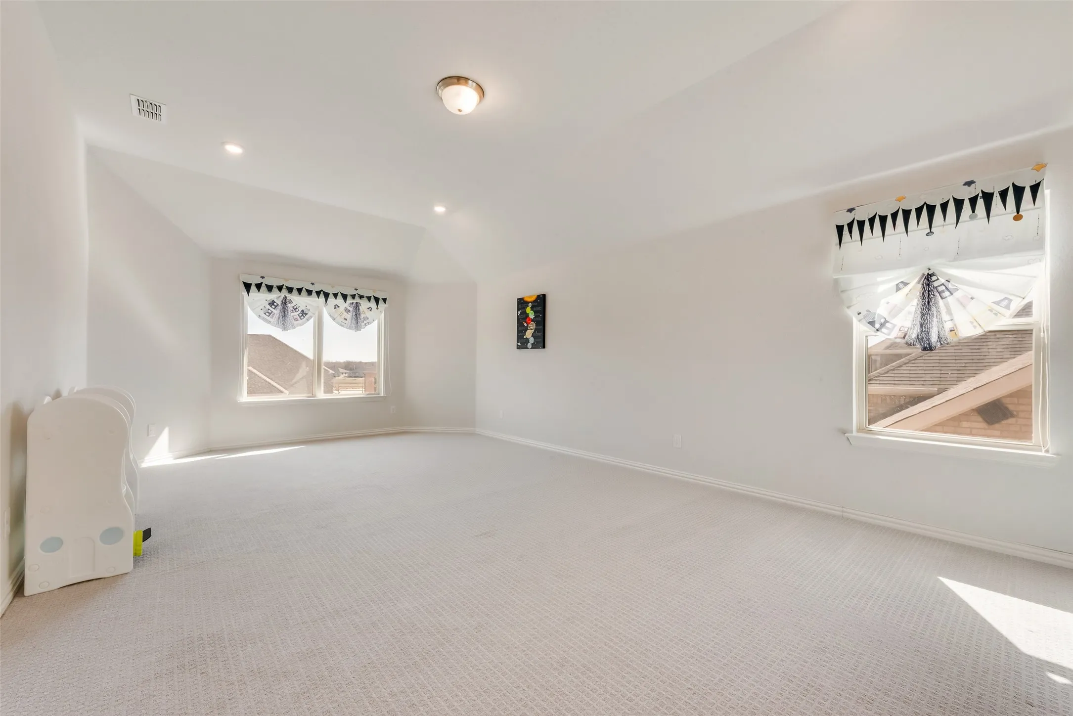 Expansive room featuring light-colored carpeting, multiple windows, and a vaulted ceiling