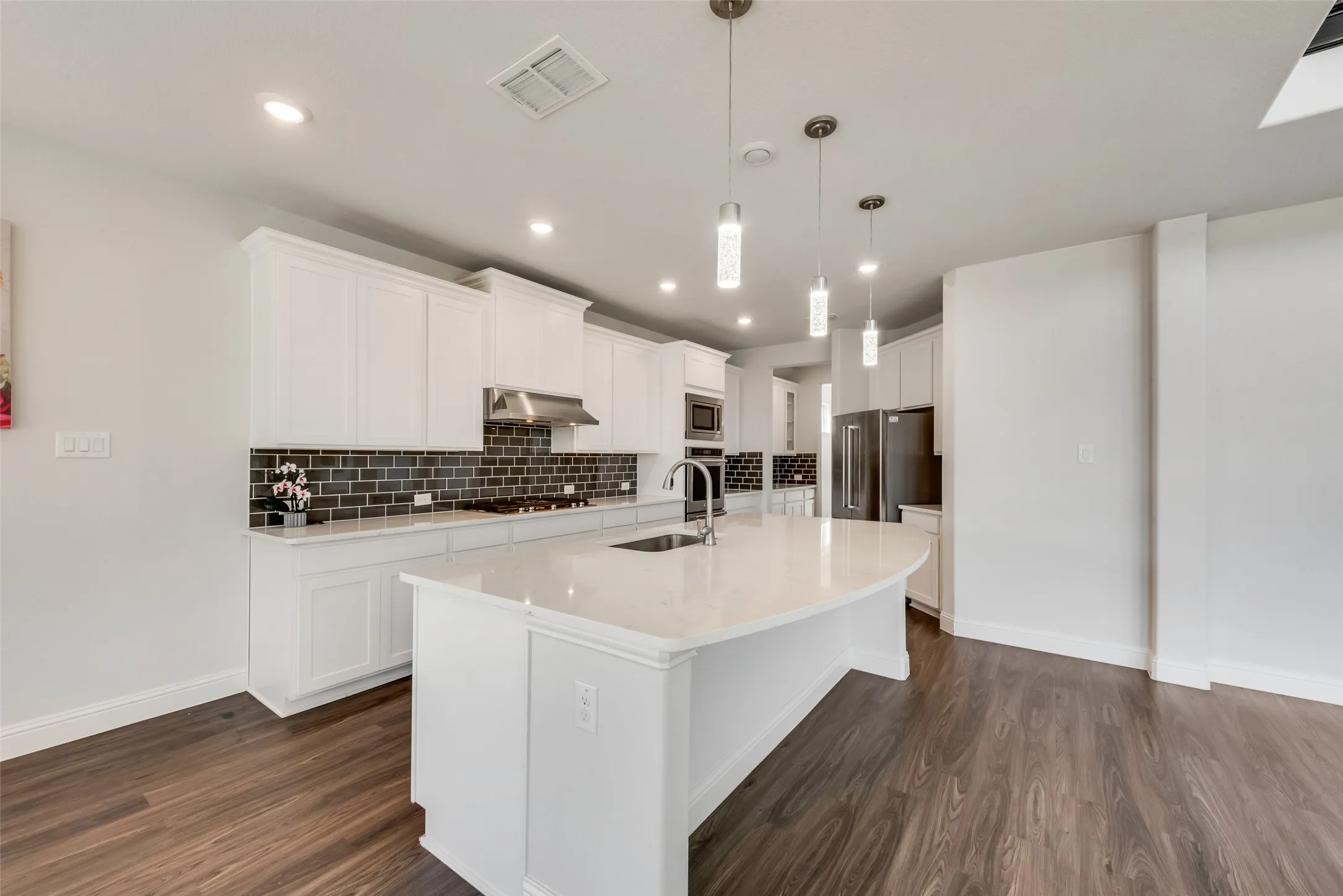 Modern kitchen featuring a large curved island with a sink and pendant lighting
