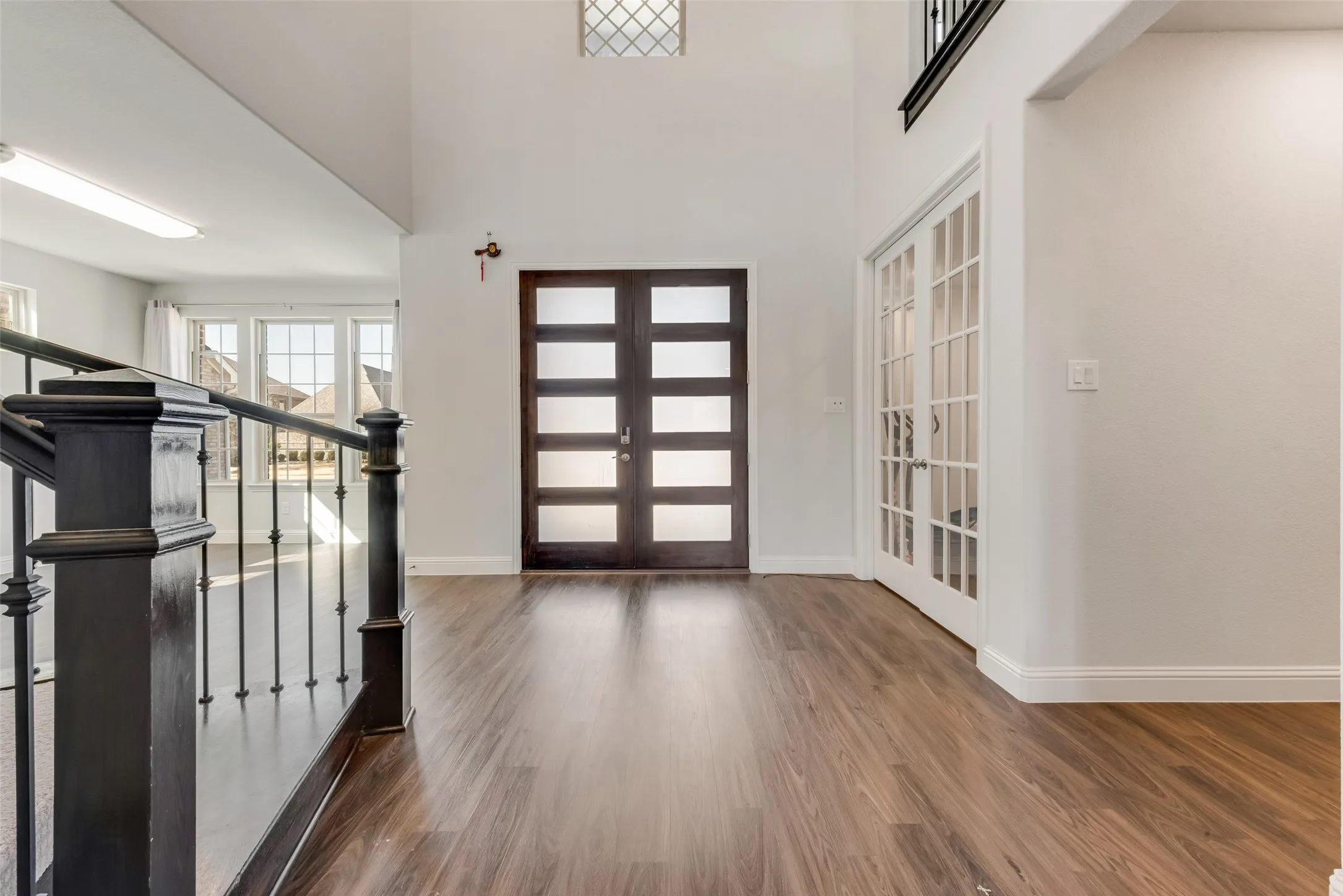 Two-story foyer featuring wood-finish flooring, a contemporary front entry door with frosted glass panels, and a grand staircase with dark wood newel posts and iron balusters