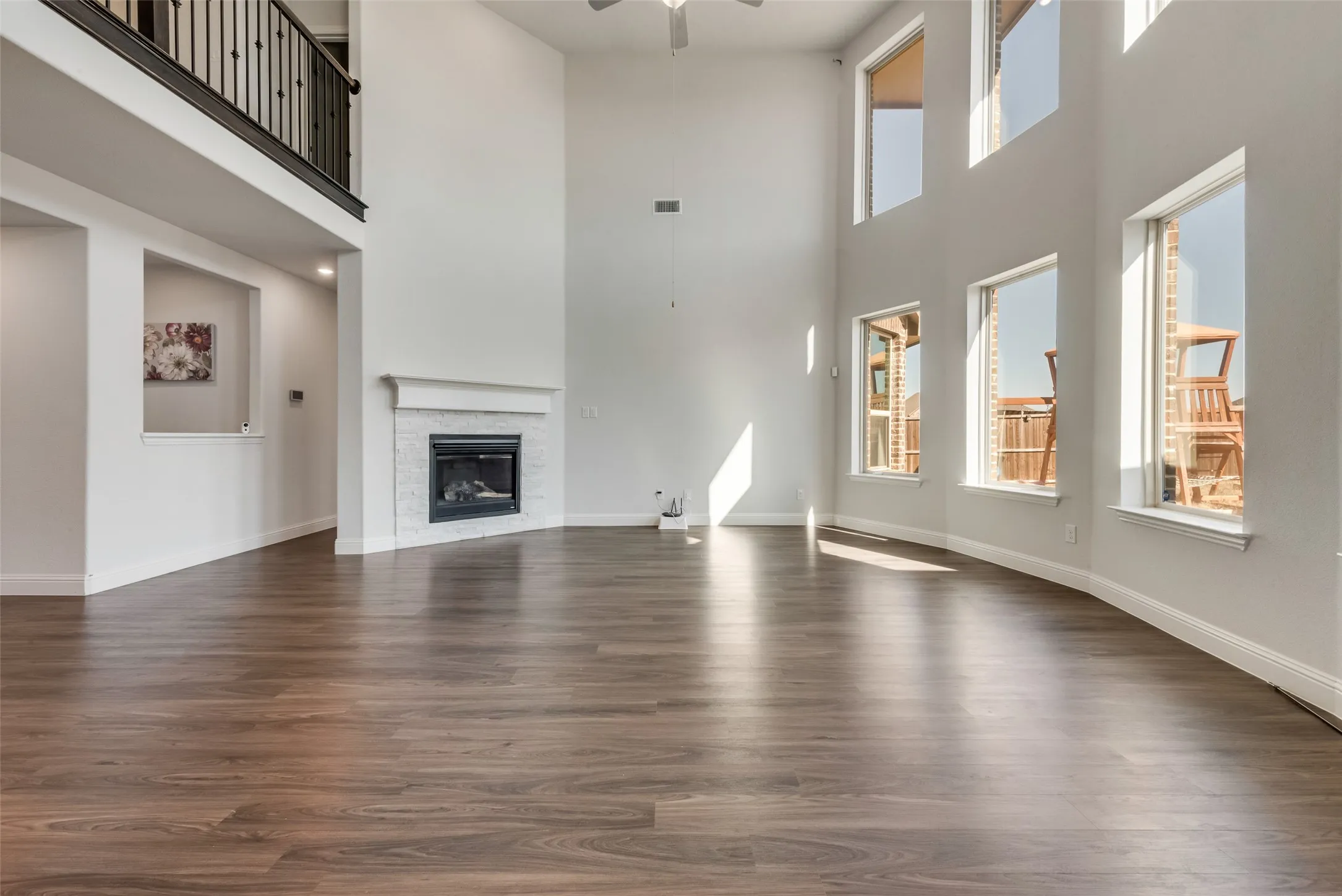 Spacious living area featuring wood-finish flooring, a white mantel fireplace with a tile surround, and an upper-level balcony with black iron railings