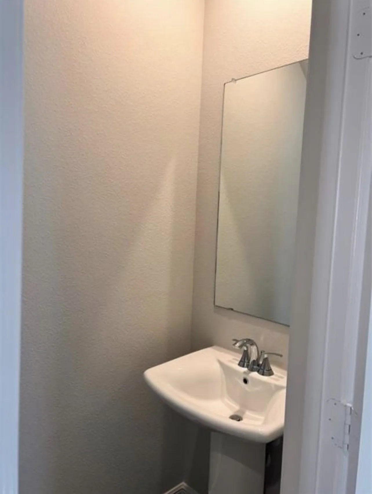 Pedestal sink with chrome faucet, complemented by a wall-mounted rectangular mirror and neutral wall finish