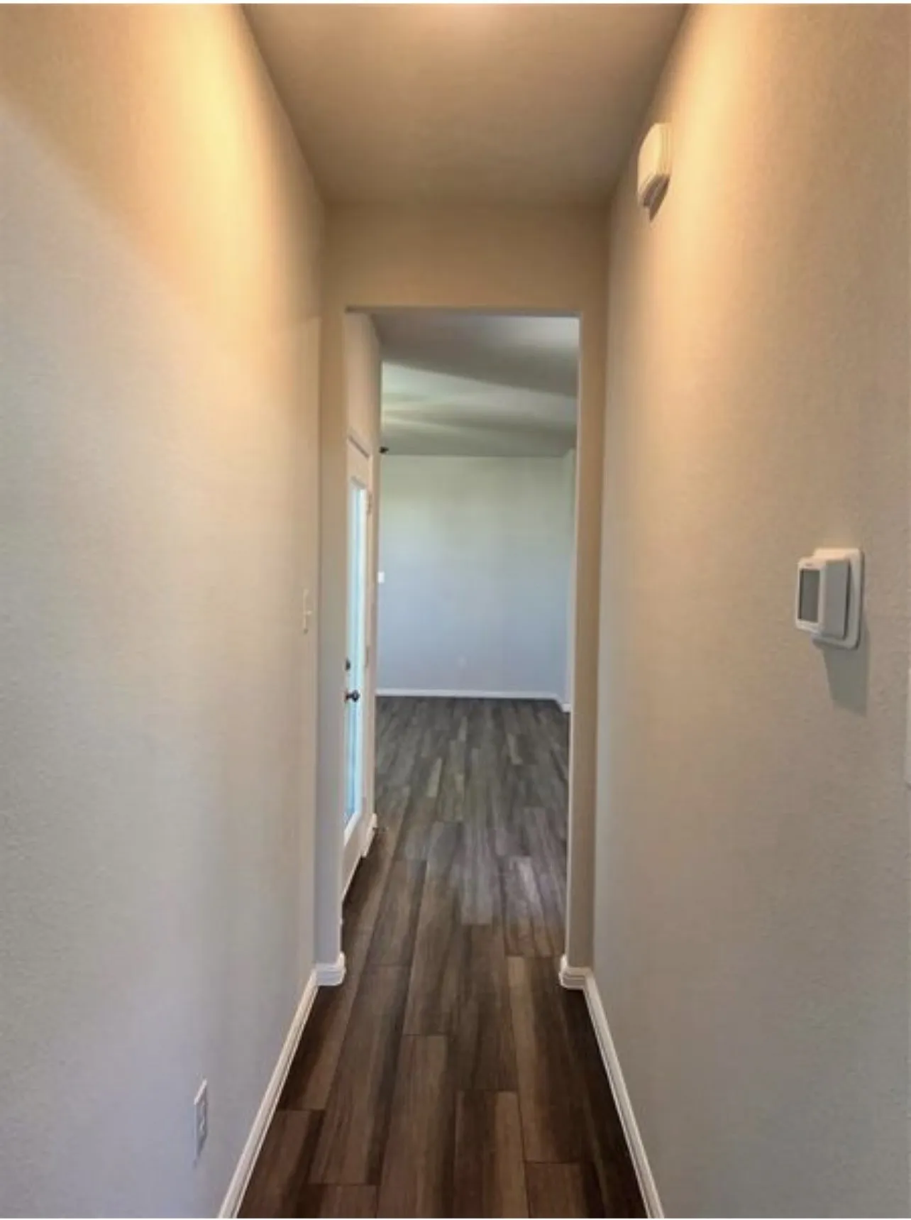 Hallway featuring wood-finish flooring, light-toned wall paint, white baseboards, and an overhead light fixture